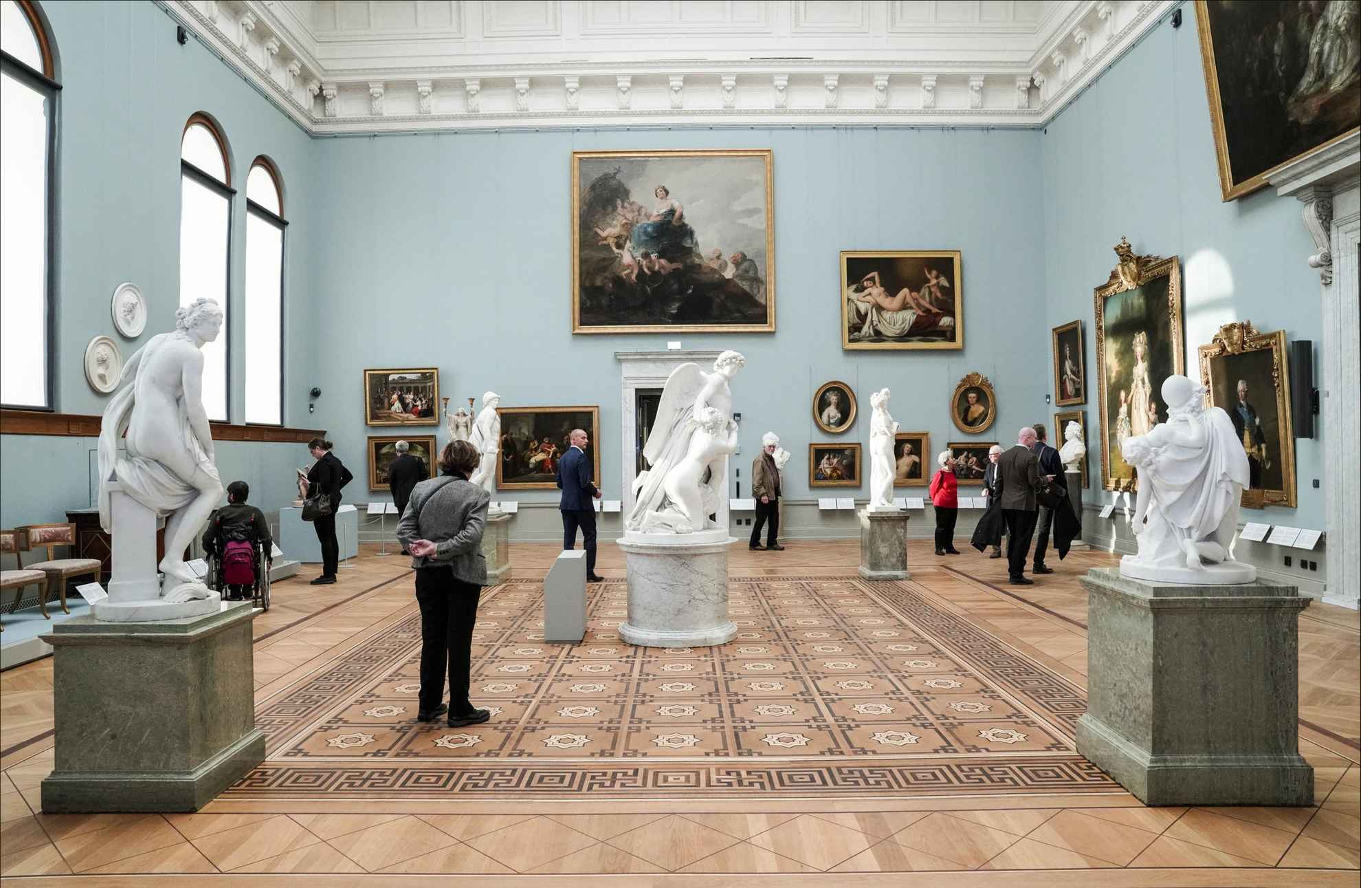 Menschen gehen in einem großen Raum mit Gemälden und Skulpturen herum.