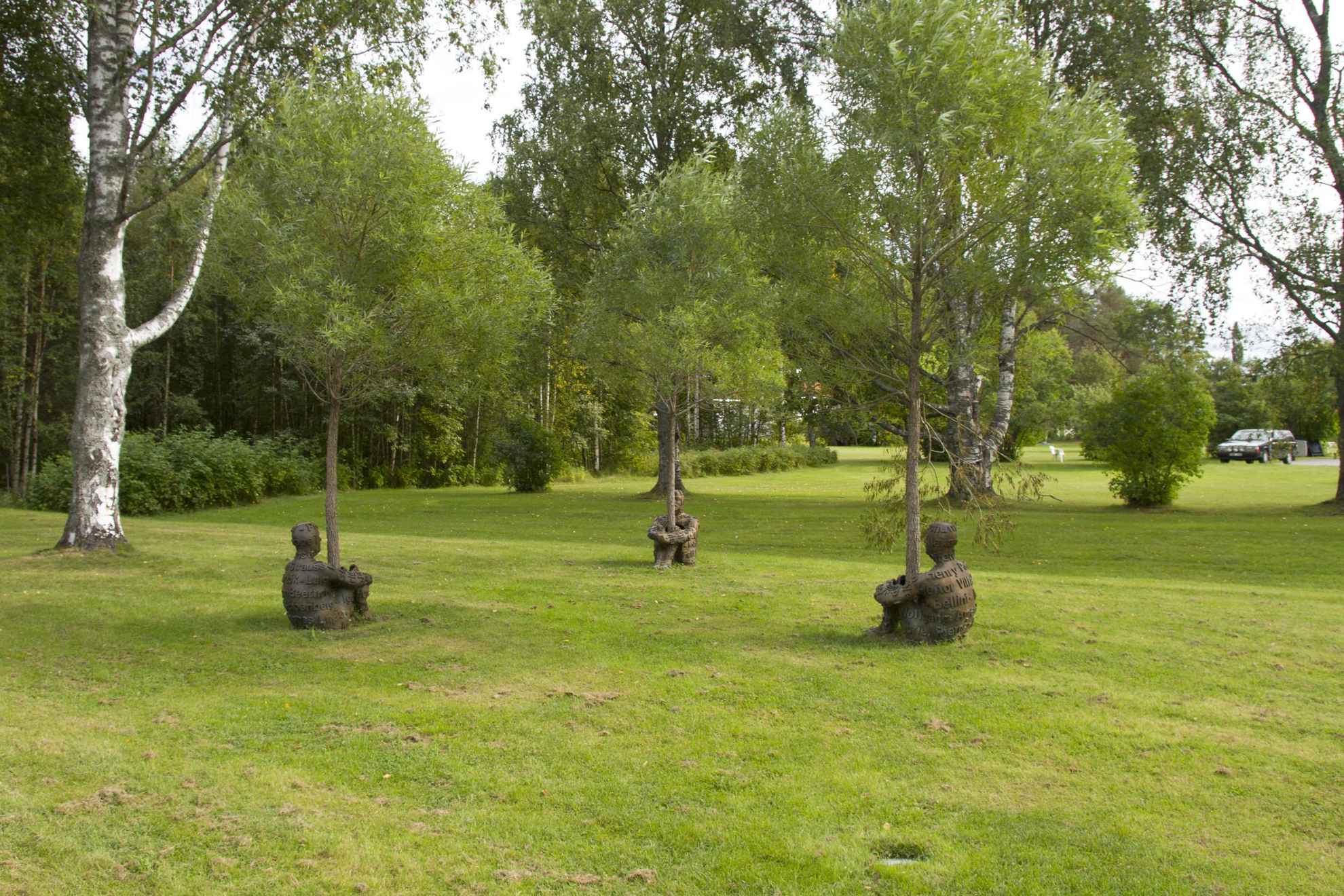 Skulpturen mit dem Namen „Heart of Trees“, drei Menschen in Bronze, die ihre Arme und Beine um einen Baumstamm geschlungen haben, in einem Skulpturenpark.