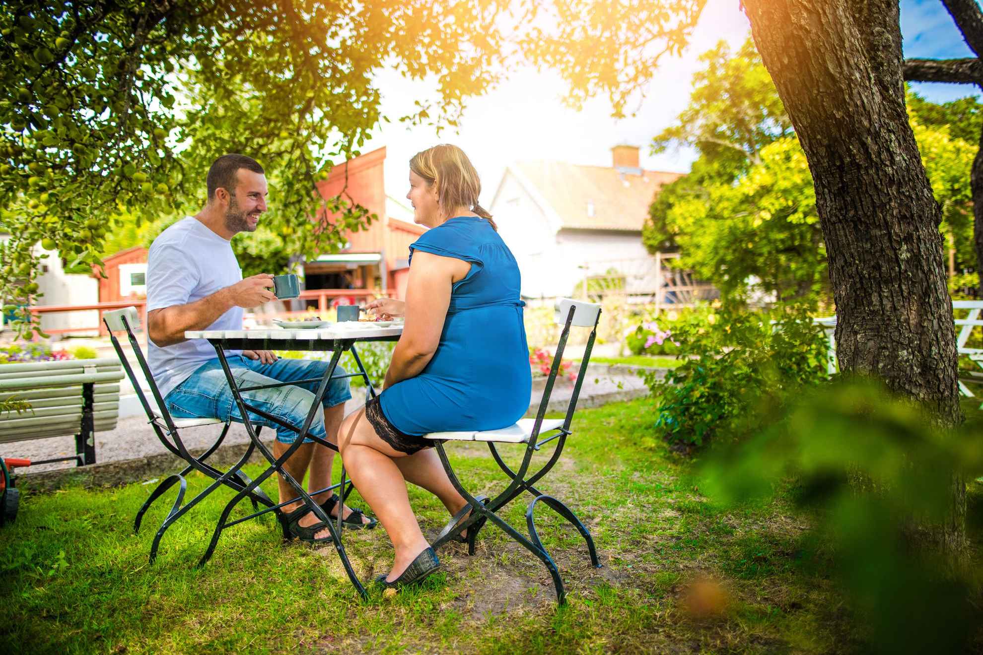 Ein Paar trinkt einen Kaffee in einem Gartencafé, umgeben von Bäumen und Grün.