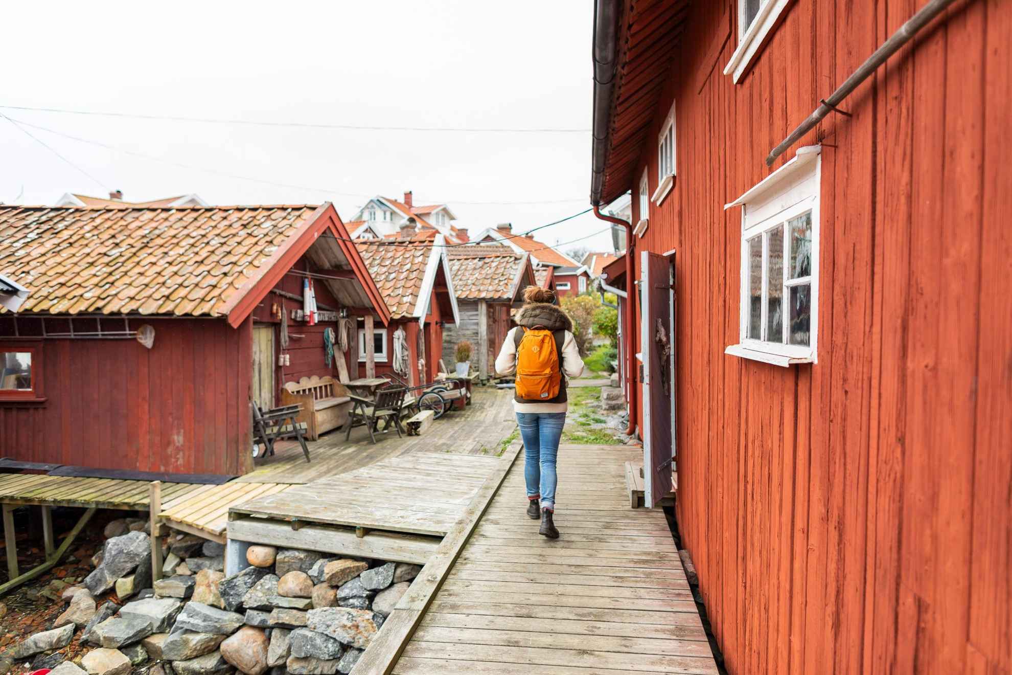 Eine Person mit einem Rucksack geht zwischen roten Holzhäusern umher.