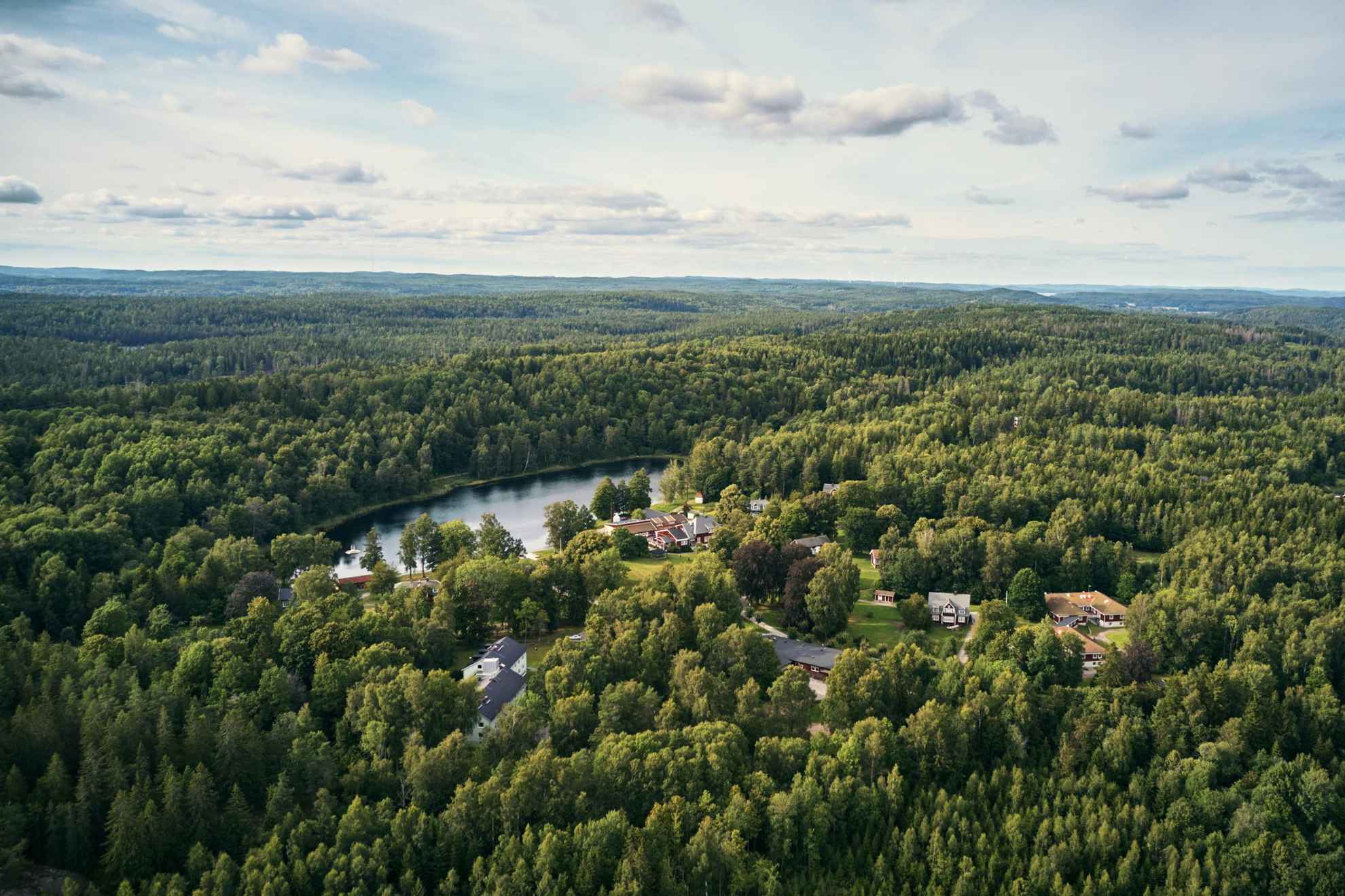 Eine Luftaufnahme des Waldes Kroppefjäll im Sommer. Zwischen den Bäumen sind ein paar Häuser zu sehen.