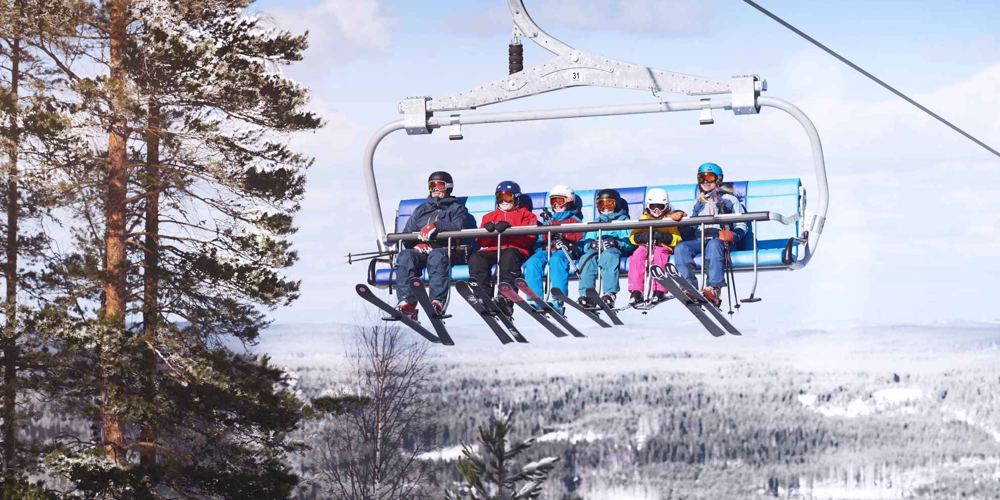 Eine sechsköpfige Familie sitzt in einem Skilift und fährt im Winter mit Skiausrüstung einen Hügel hinauf.