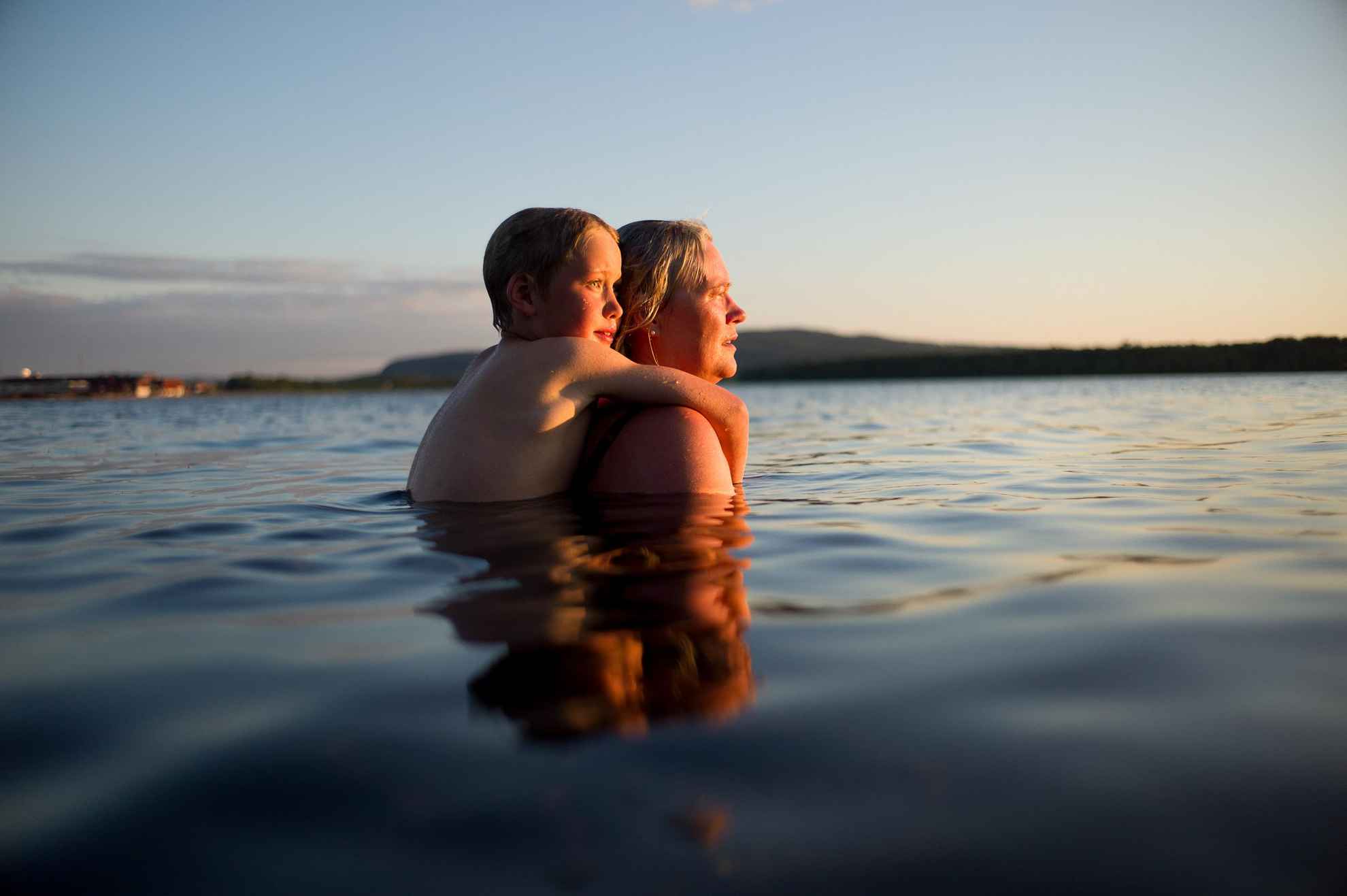 A woman and a child are in the water in a lake in Dalarna. The child is holding on to the woman's back.