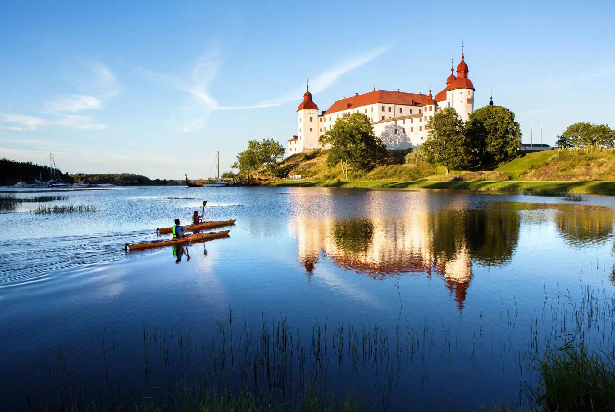 Zwei Personen, die im Sommer auf einem See vor einem großen weißen Schloss Kajak fahren.