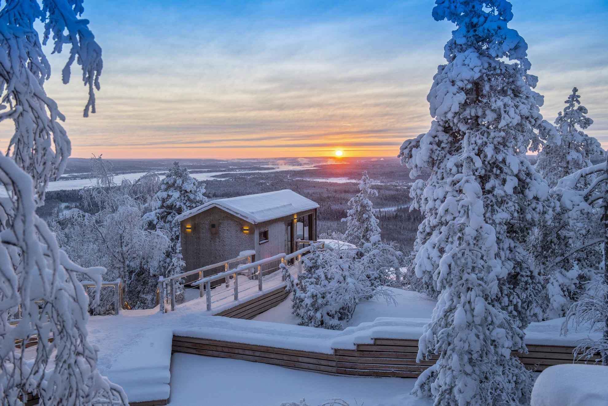Ein verschneites Chalet in der Lapland View Lodge, während die Sonne untergeht.