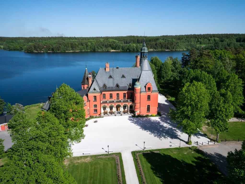 Ein Schloss mit roter Fassade ist von Grünflächen und einem See umgeben.