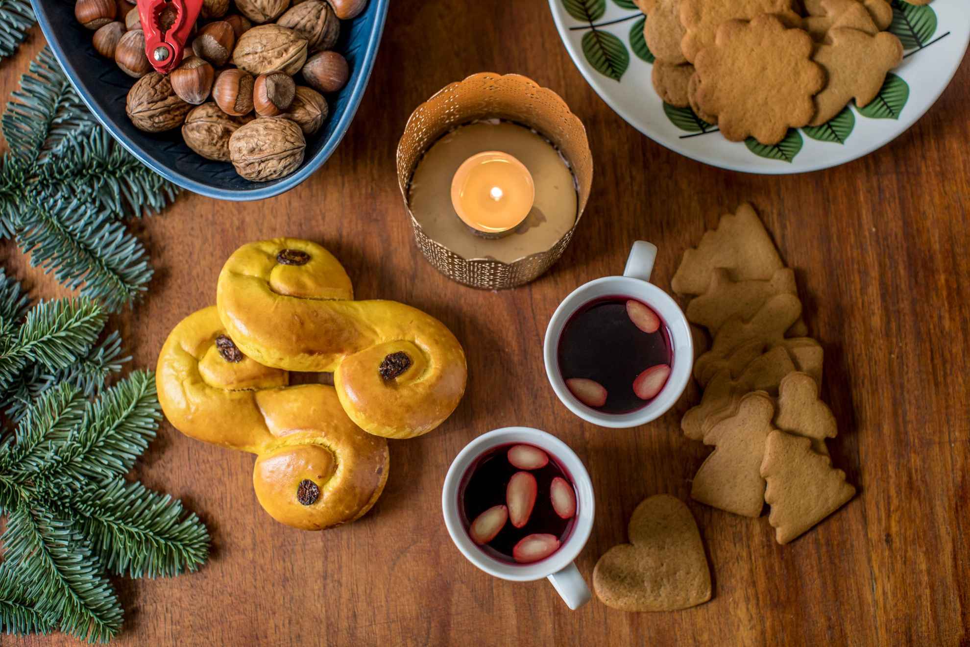 Ein Tisch mit typisch schwedischen Weihnachtsleckereien und -dekorationen, Glühwein, Nüssen, Lebkuchen, Lussebullar und Tannenzweigen.