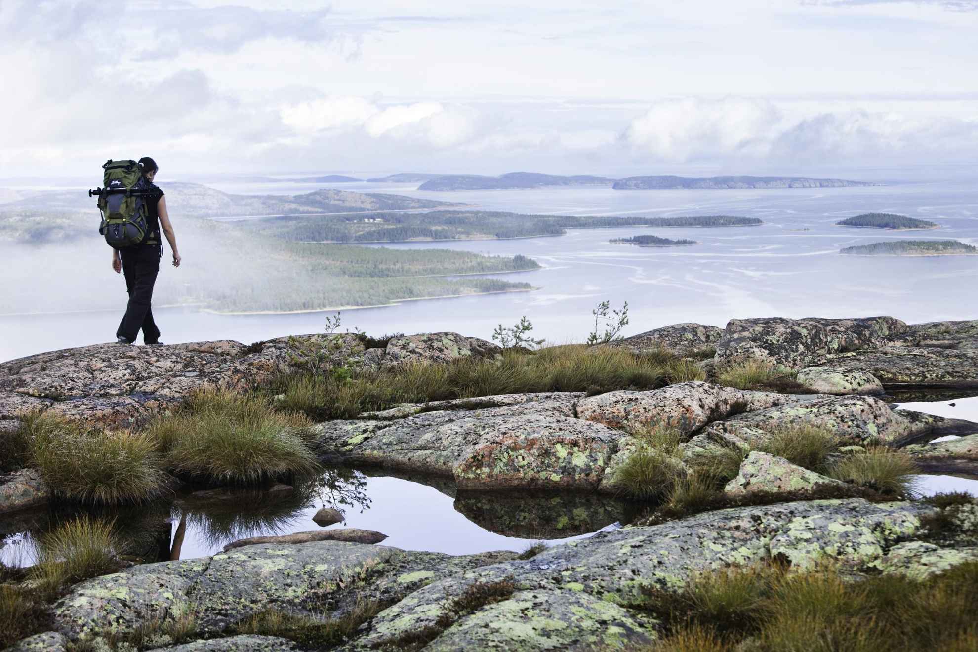 Eine Person mit Rucksack wandert auf einem Hügel mit Blick auf das Meer und die Schären an der hohen Küste.