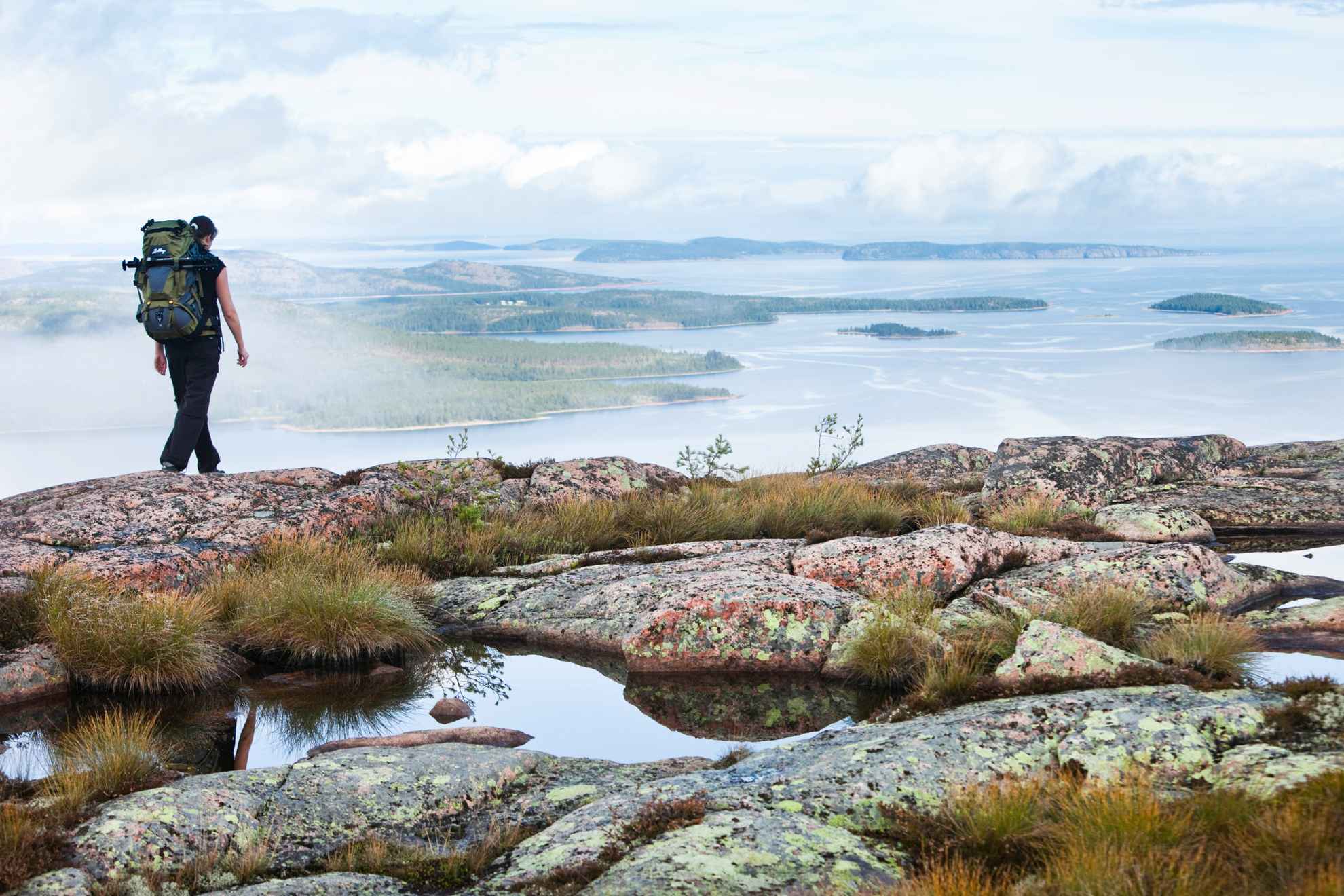 A person with a backpack hiking on a hill with a view over the sea and the archipelago at the high coast.