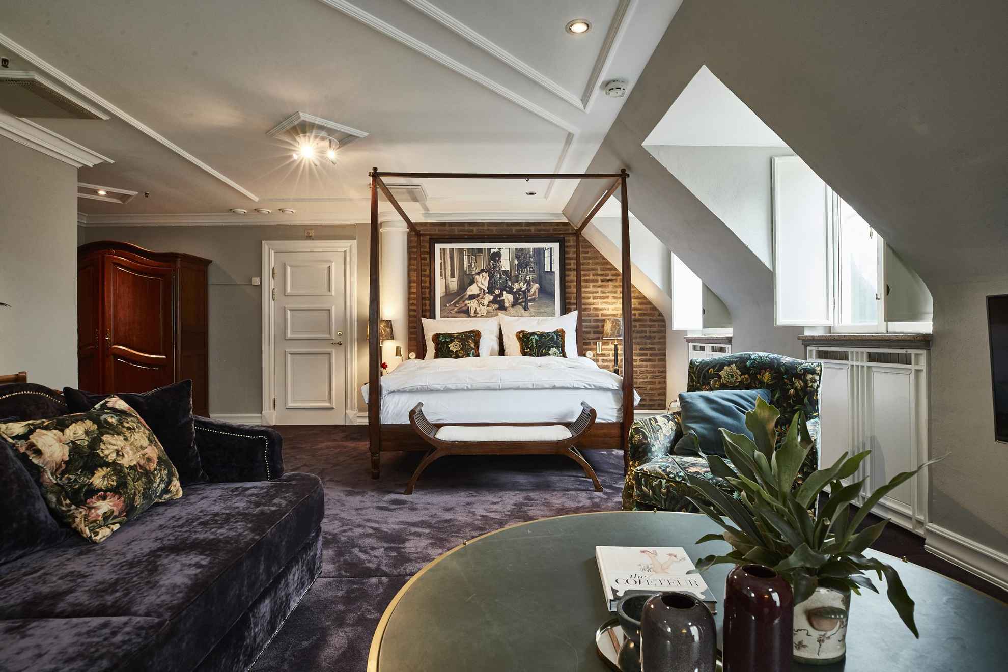 Ein großes Hotelzimmer mit Samtteppich und Sofa, einem grünen Couchtisch, einem Doppelbett und einem Holzschrank.