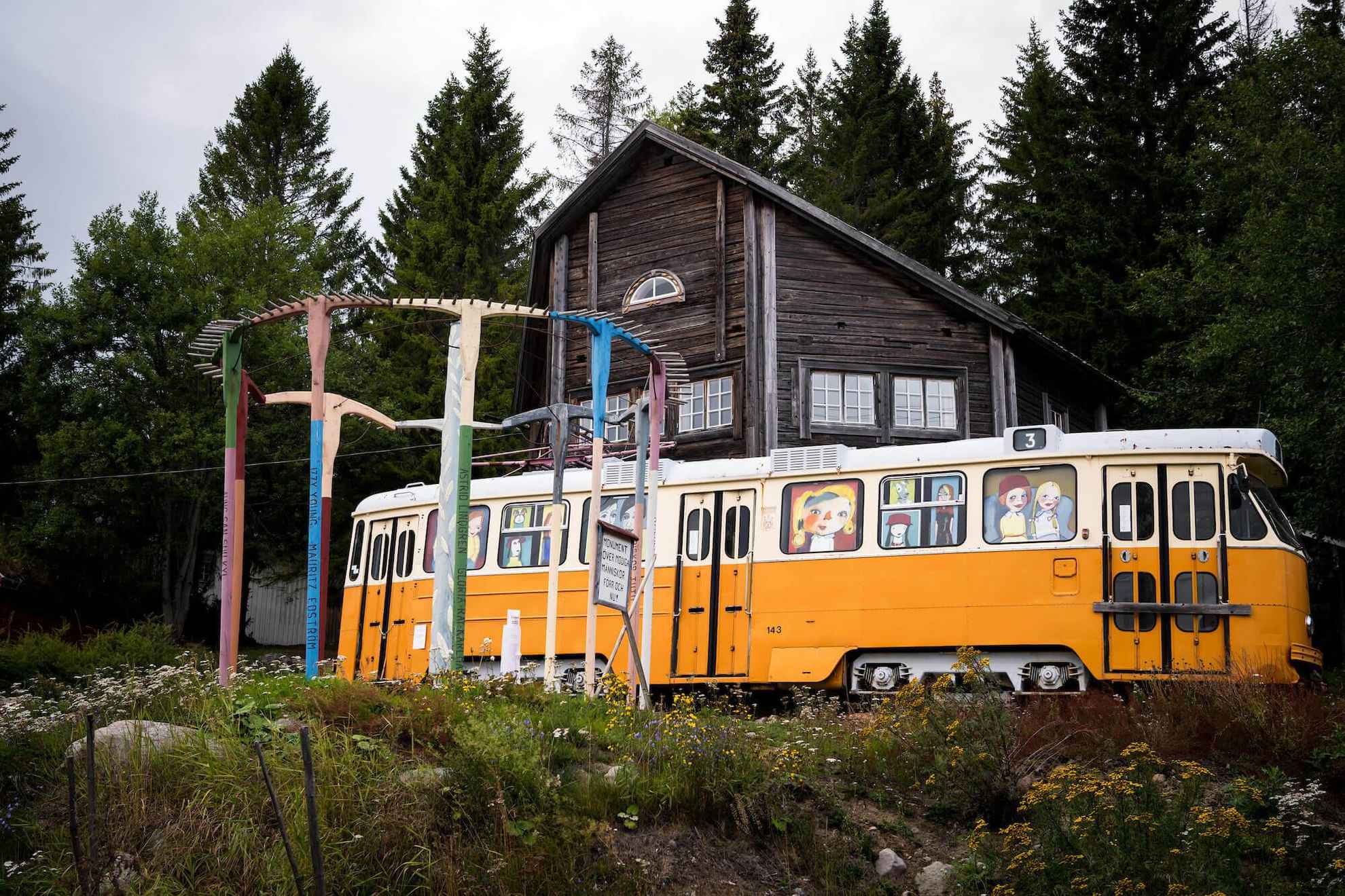 Eine alte gelbe Straßenbahn ist draußen in der Natur. In den Fenstern gibt es Cartoon-Bilder von Kindern.