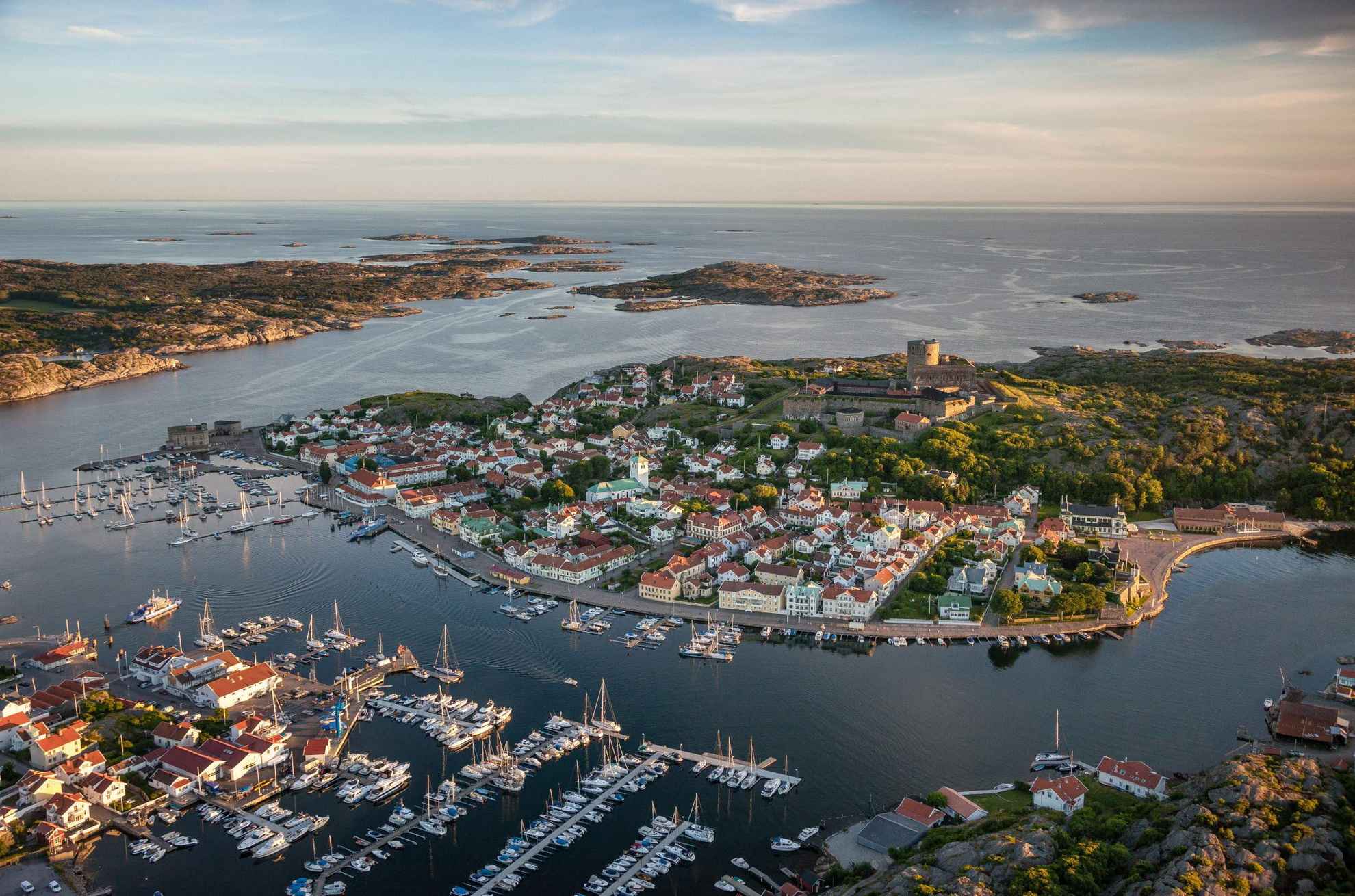 Luftaufnahme der kleinen Stadt Marstrand mit vielen Segelbooten im Vordergrund, der Festung auf der Insel in der Mitte und dem Schärengarten im Hintergrund.
