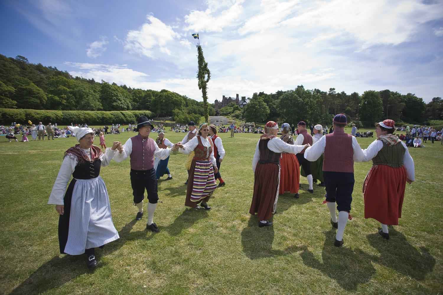 Menschen in traditioneller Kleidung tanzen um einen Maibaum während des Mittsommerfests auf dem Schloss Tjolöhölm in Halland