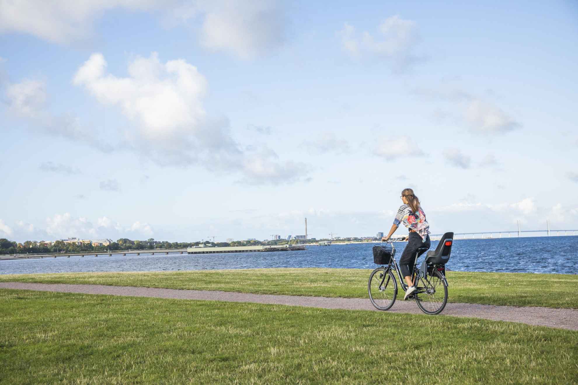 Eine Frau fährt mit ihrem Fahrrad auf einem Radweg entlang der Küste im Westhafen.