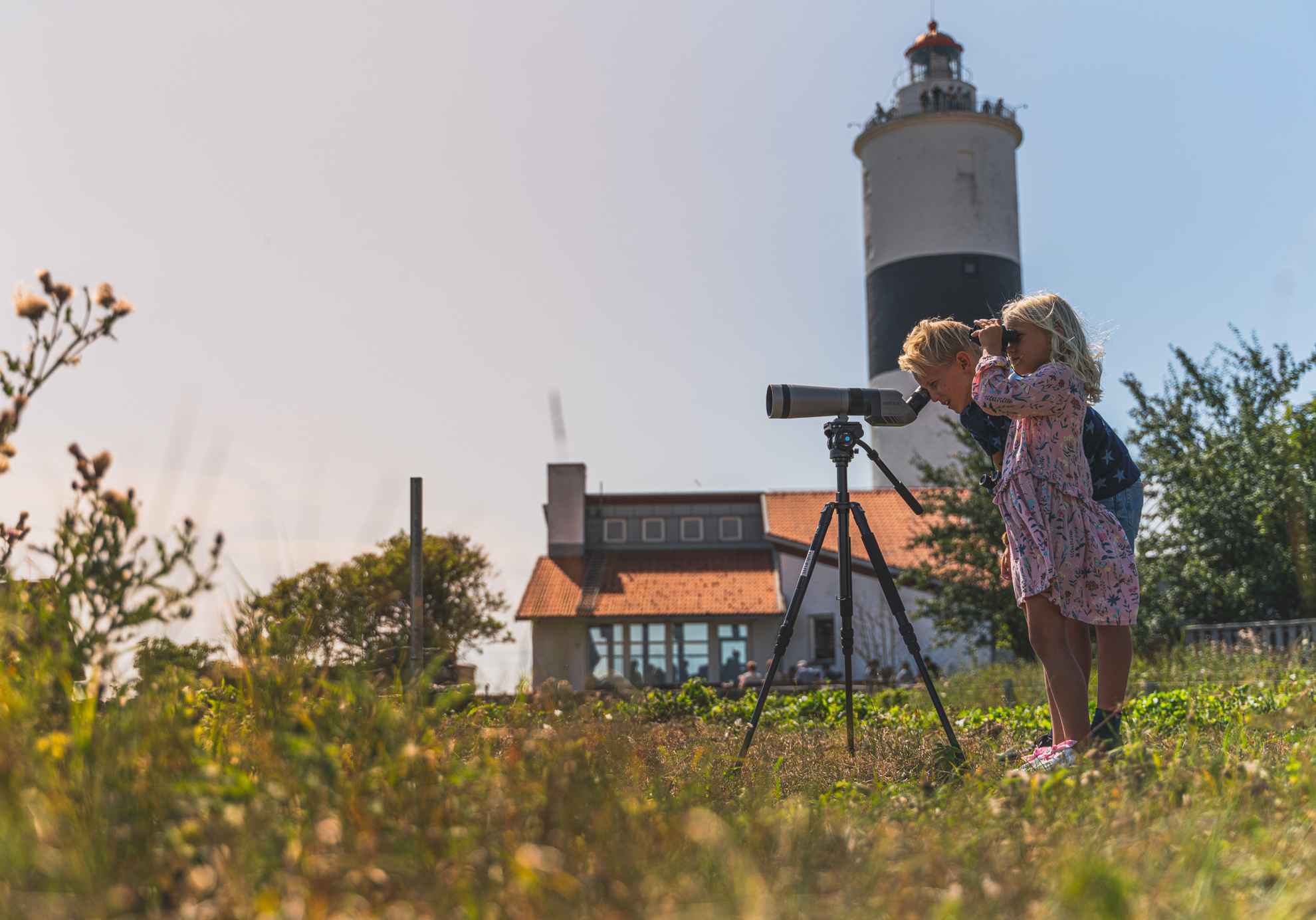 Ein Mädchen und ein Junge beobachten Vögel durch ein Fernrohr am Leuchtturm Långe Jan auf Öland
