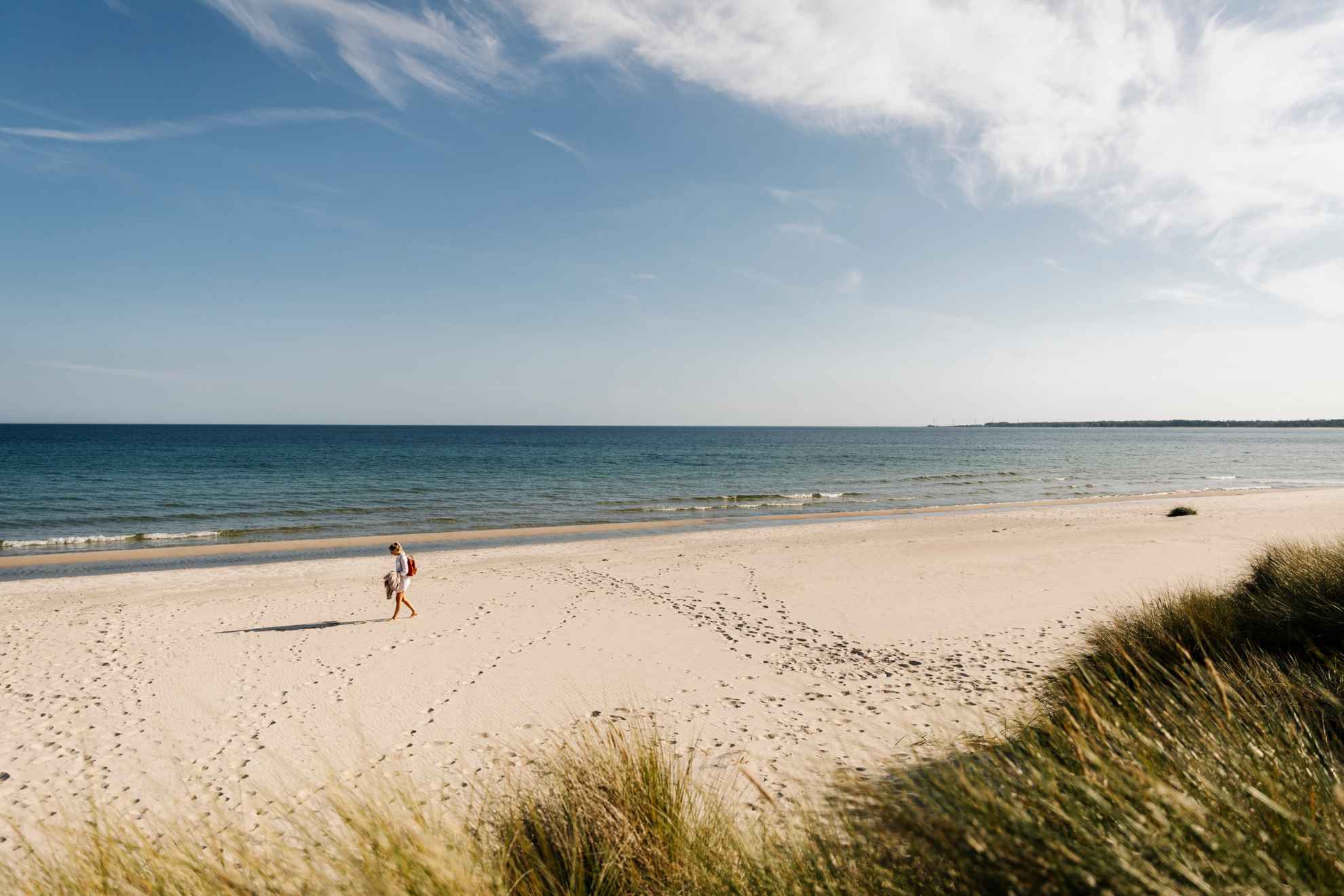 Eine Person geht am Böda Sandstrand spazieren. Das Meer und der blaue Himmel sind im Hintergrund.