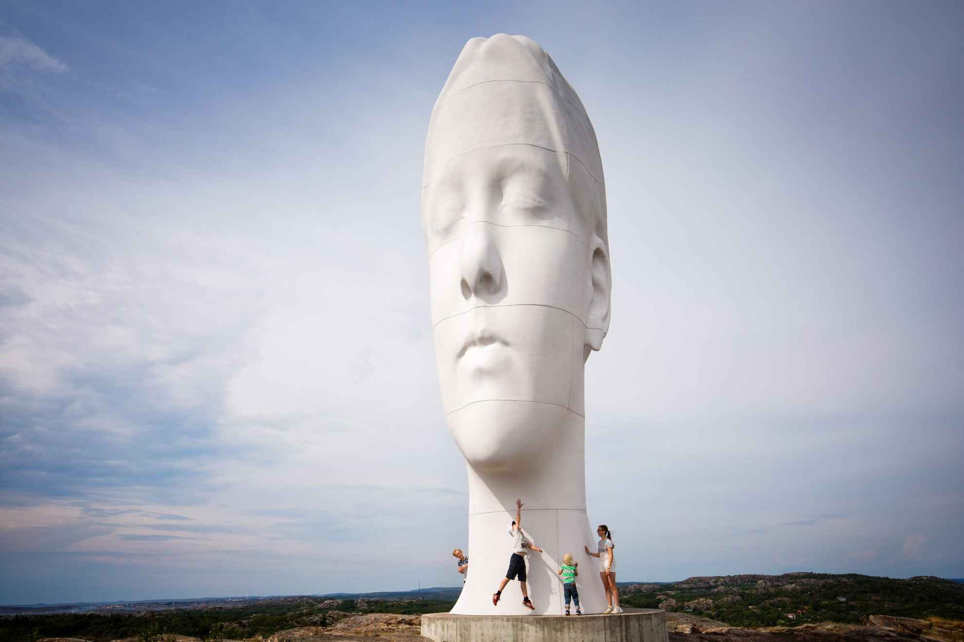 Eine große Statue in Form eines menschlichen Kopfes, die mitten in der Natur steht, und vier Menschen, die direkt darunter stehen.