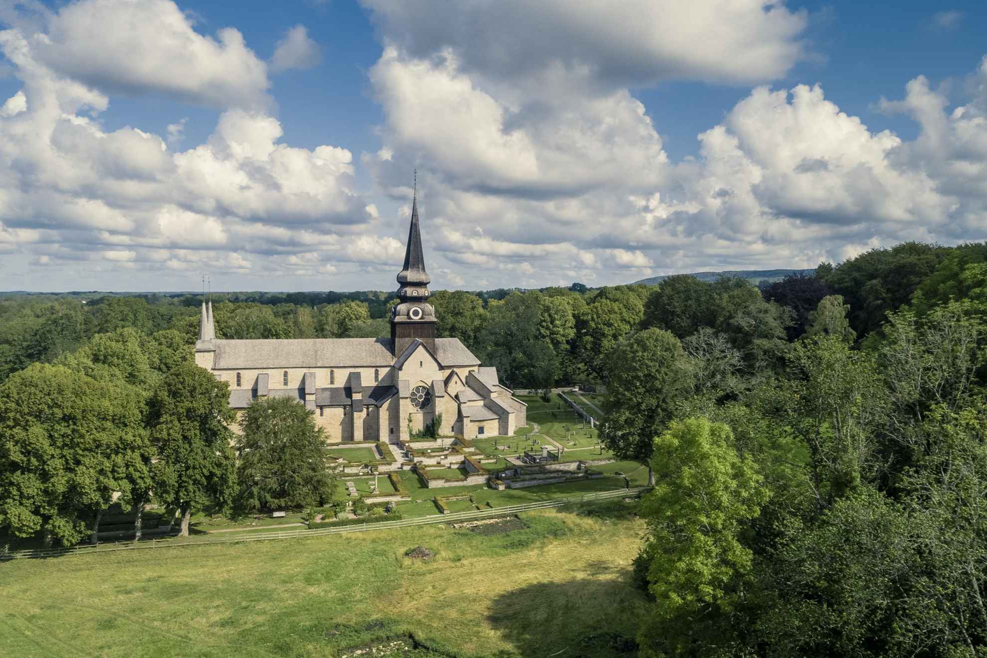 Luftaufnahme einer mittelalterlichen Kirche, ihres Friedhofs und der umliegenden Felder und Wälder.