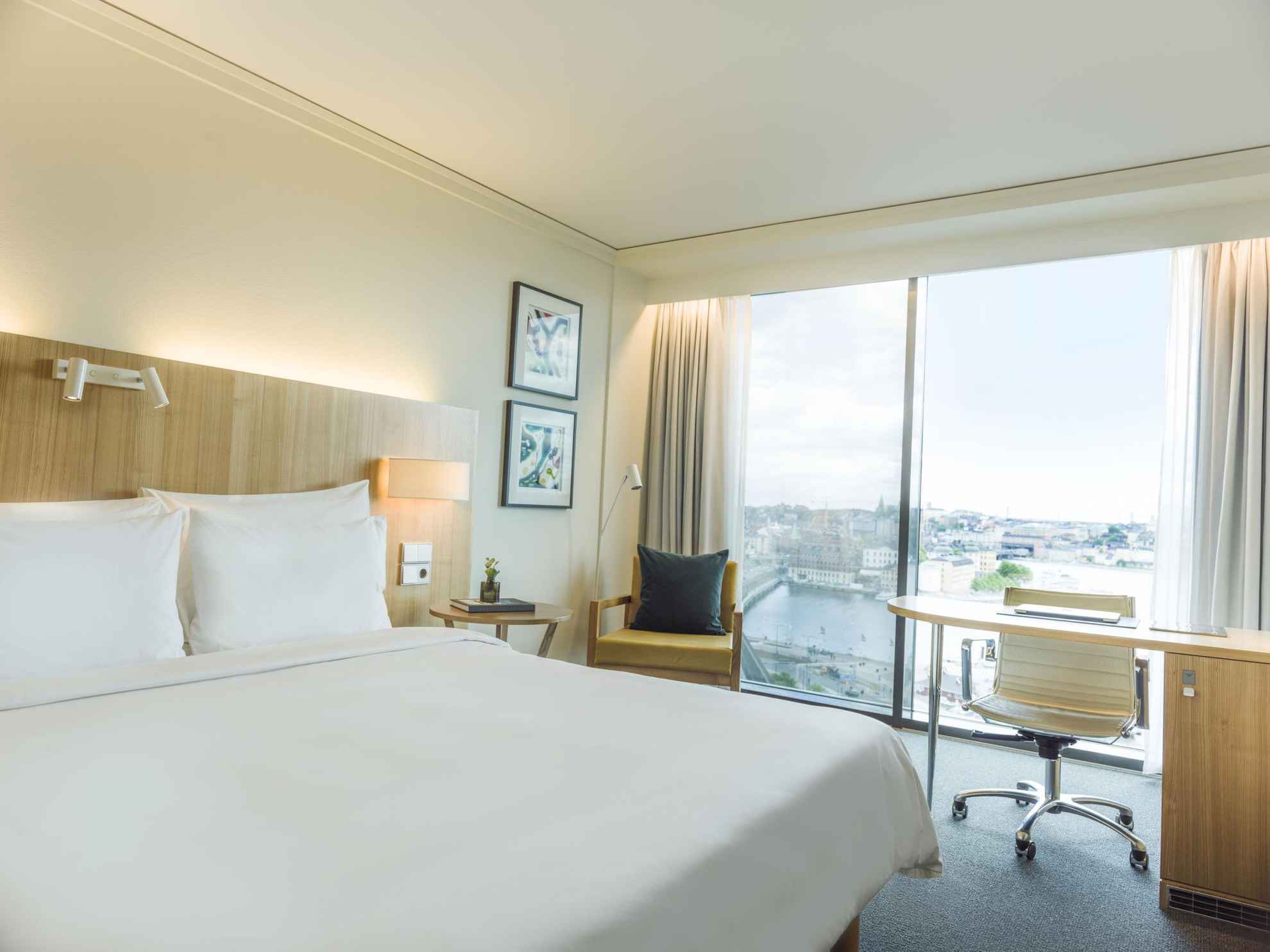 Ein Premium-Hotelzimmer des Radisson Blu Waterfront Hotel, Stockholm mit einem Doppelbett mit weißer Bettwäsche. Große Fenster mit Blick auf das Wasser.