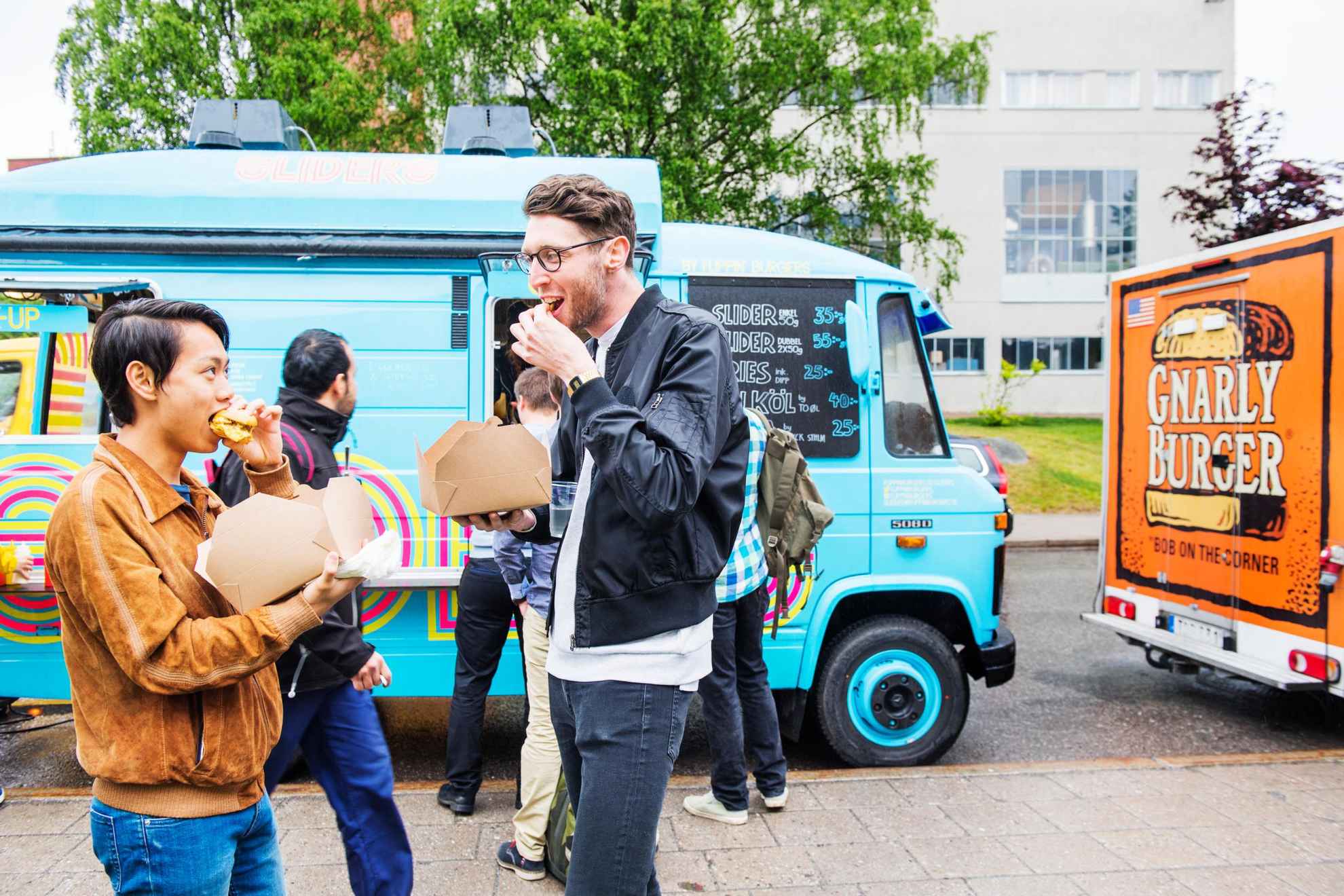 Freunde essen Fingerfood aus Kartons neben einem in Stockholm geparkten Imbisswagen.
