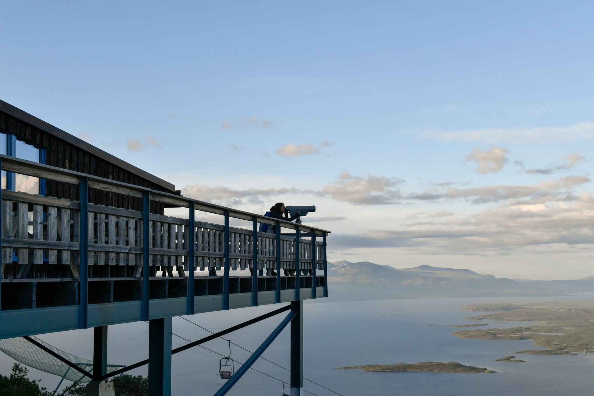 Jemand benutzt das große Fernglas in der STF Abisko Turiststation, die hoch über dem Boden liegt und einen Blick auf Berge und Seen bietet.