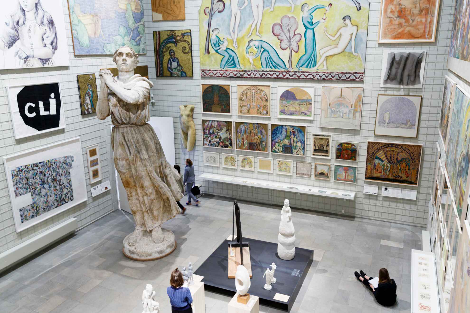 Ein Museumsraum mit einer großen und zahlreichen kleinen Skulpturen sowie bunten Skizzen an der Wand.