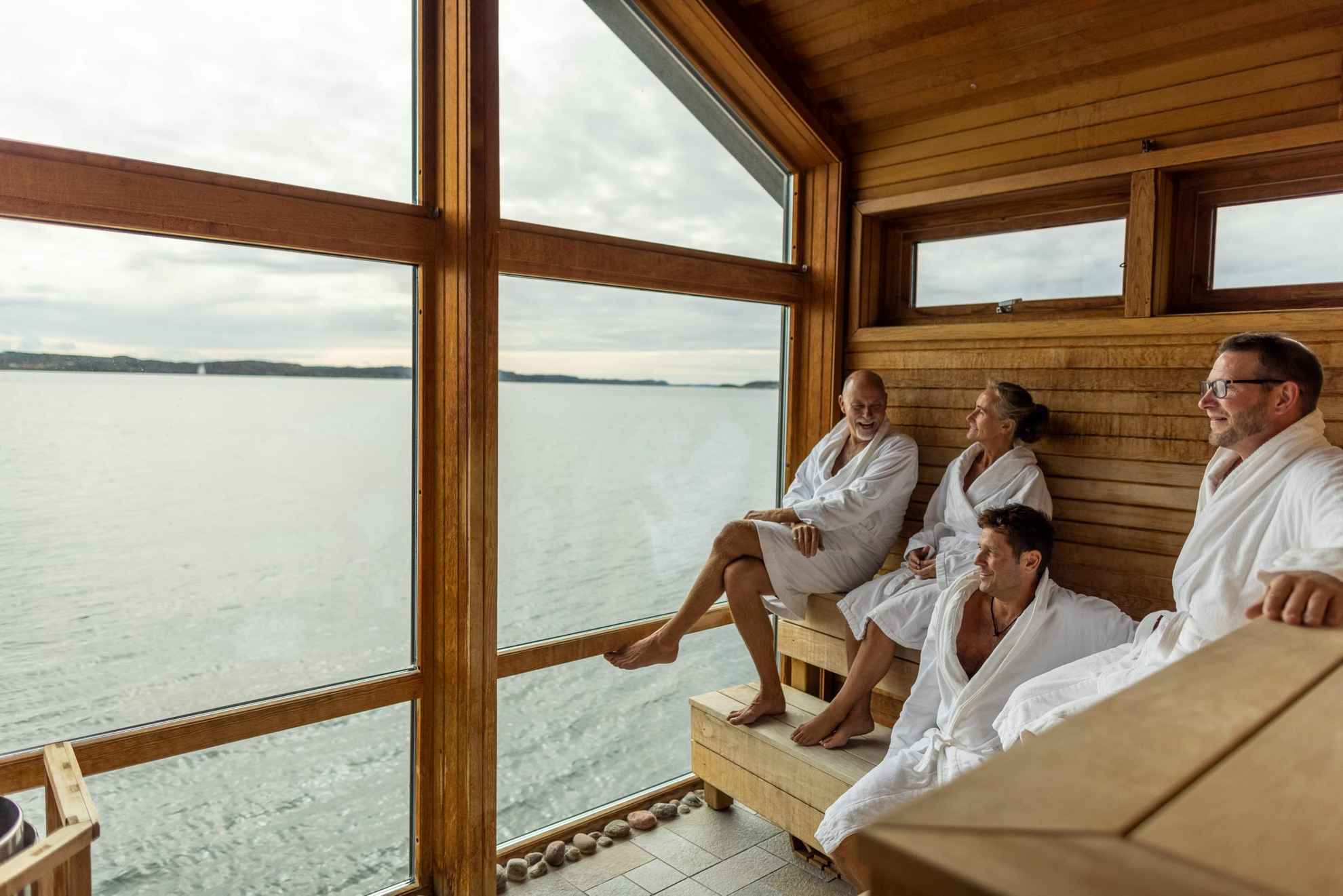 Vier Personen genießen die Sauna und den Blick auf das Meer.