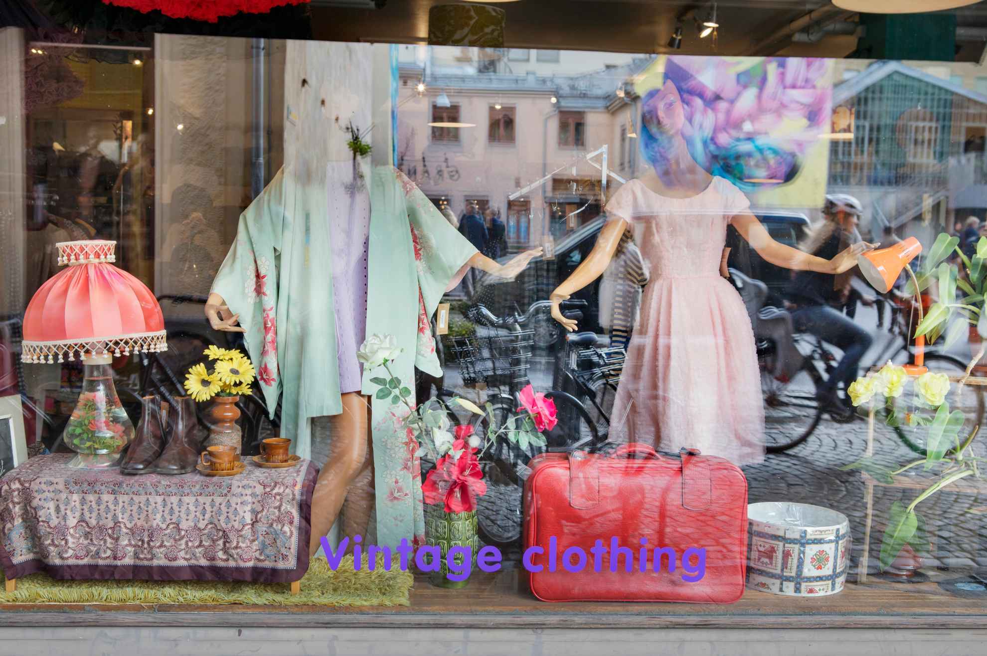 Ein Schaufenster mit Vintage-Kleidung. Du kannst Spiegelungen im Fenster von Menschen sehen, die sich bewegen.