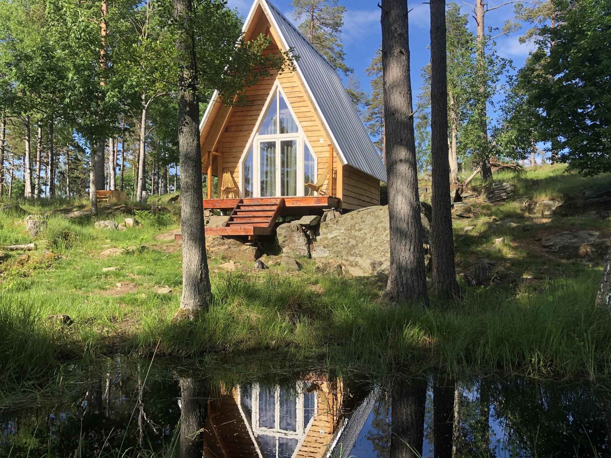 Eine Hütte mit großen Fenstern steht in der grünen, schwedischen Landschaft.
