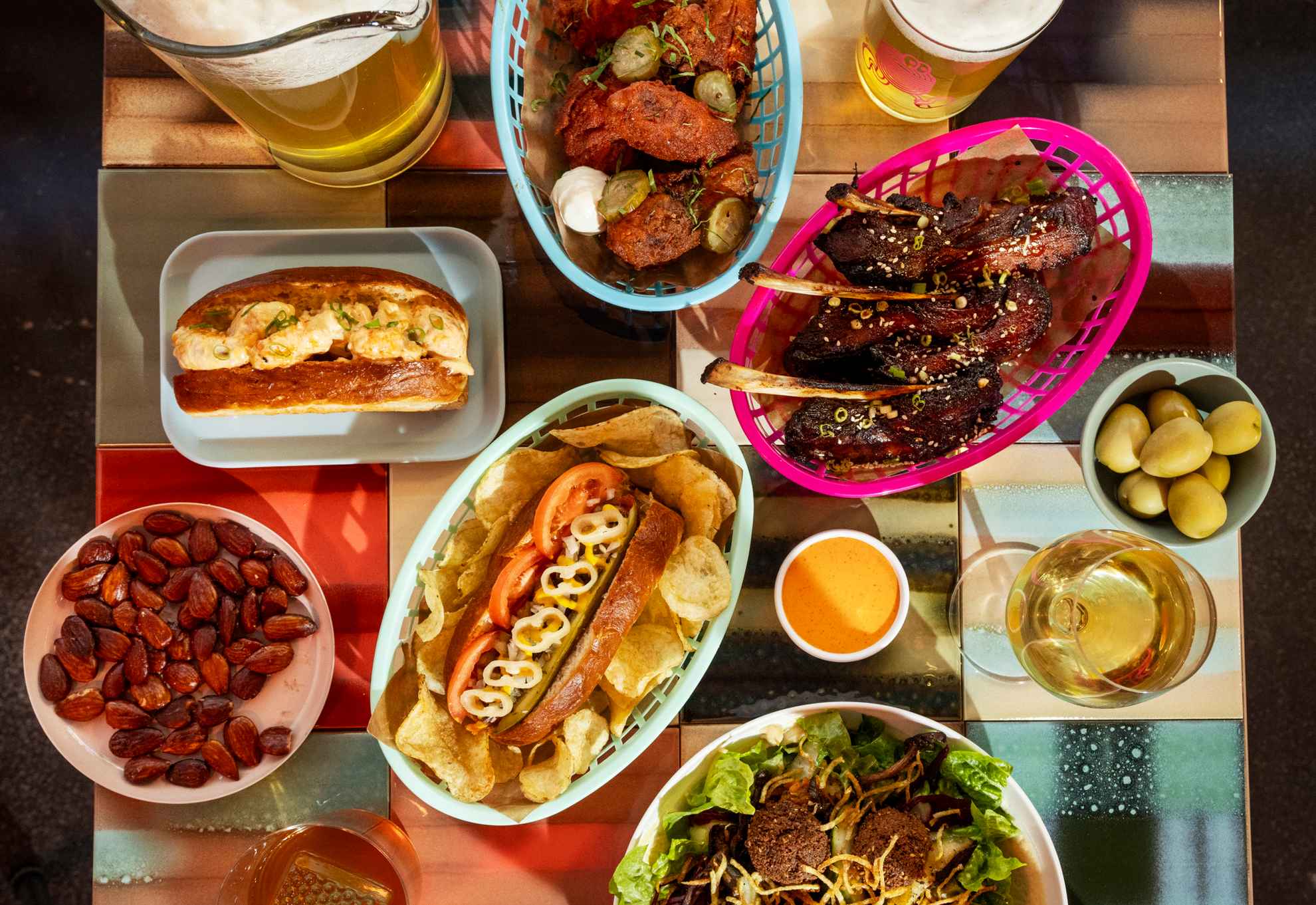 Ein quadratischer Tisch, gefüllt mit buntem Streetfood in verschiedenen Körben und auf Tellern, sowie Gläsern mit Bier und Wein.