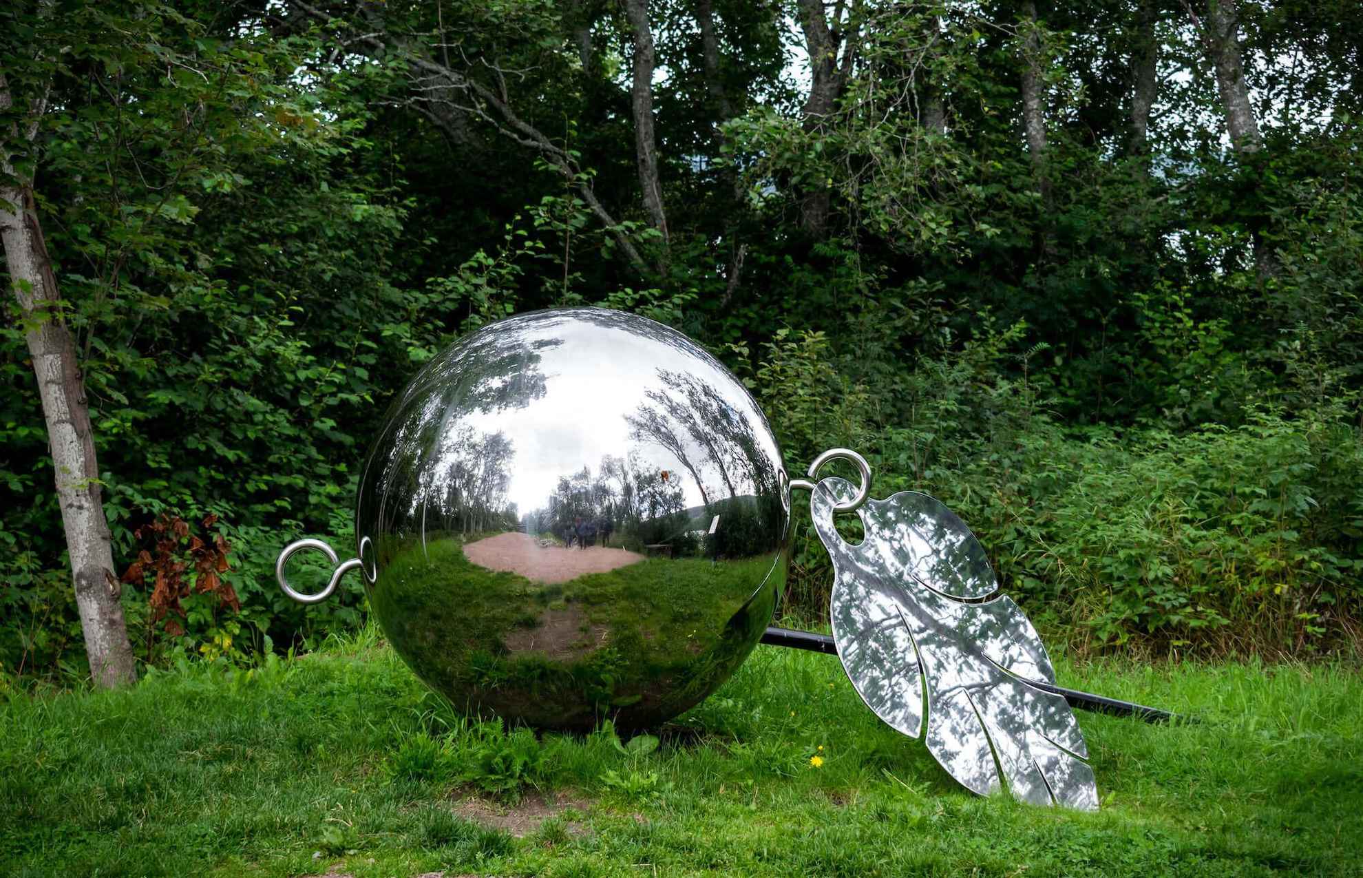 Ein Kunstwerk einer reflektierenden Metallkugel steht in der Natur.