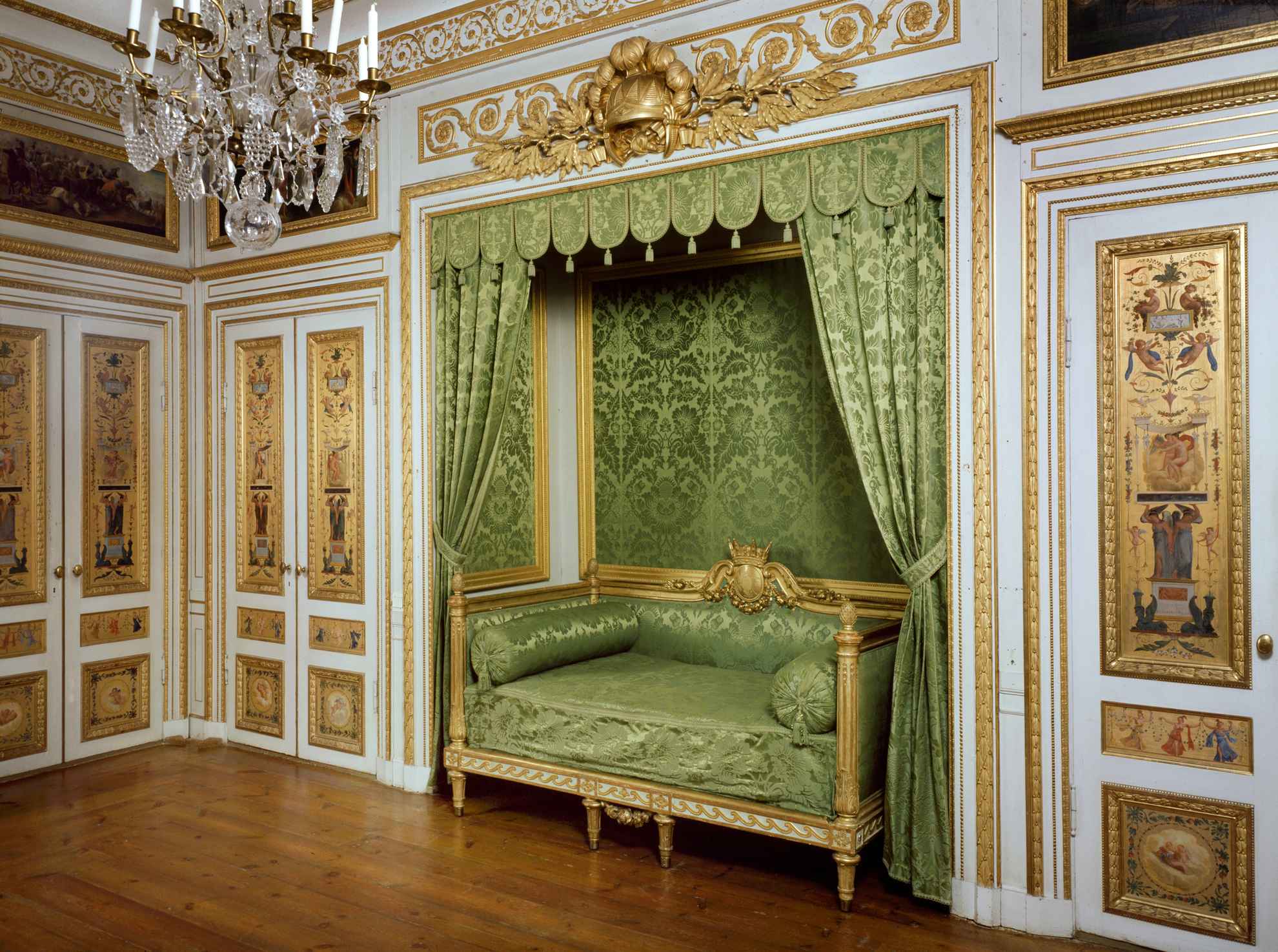 Ein Schlafzimmer im Palais Tullgarn mit grünem Sofa, goldenen Wänden und Kronleuchter.