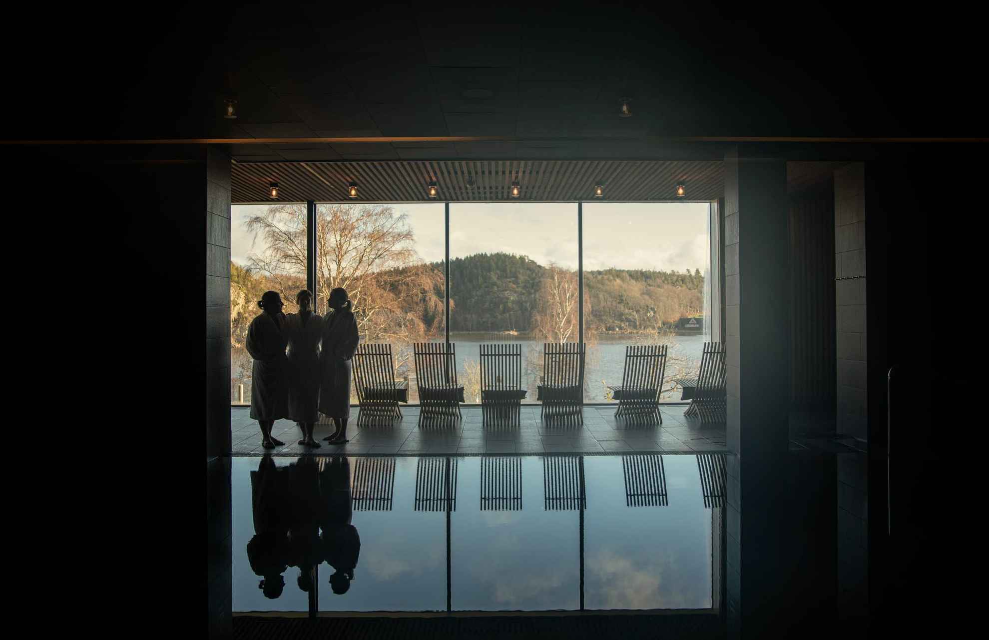 Gäste des Vann Spas laufen an einem Pool vorbei und blicken durch das Panorama Fenster auf die schwedische Landschaft.