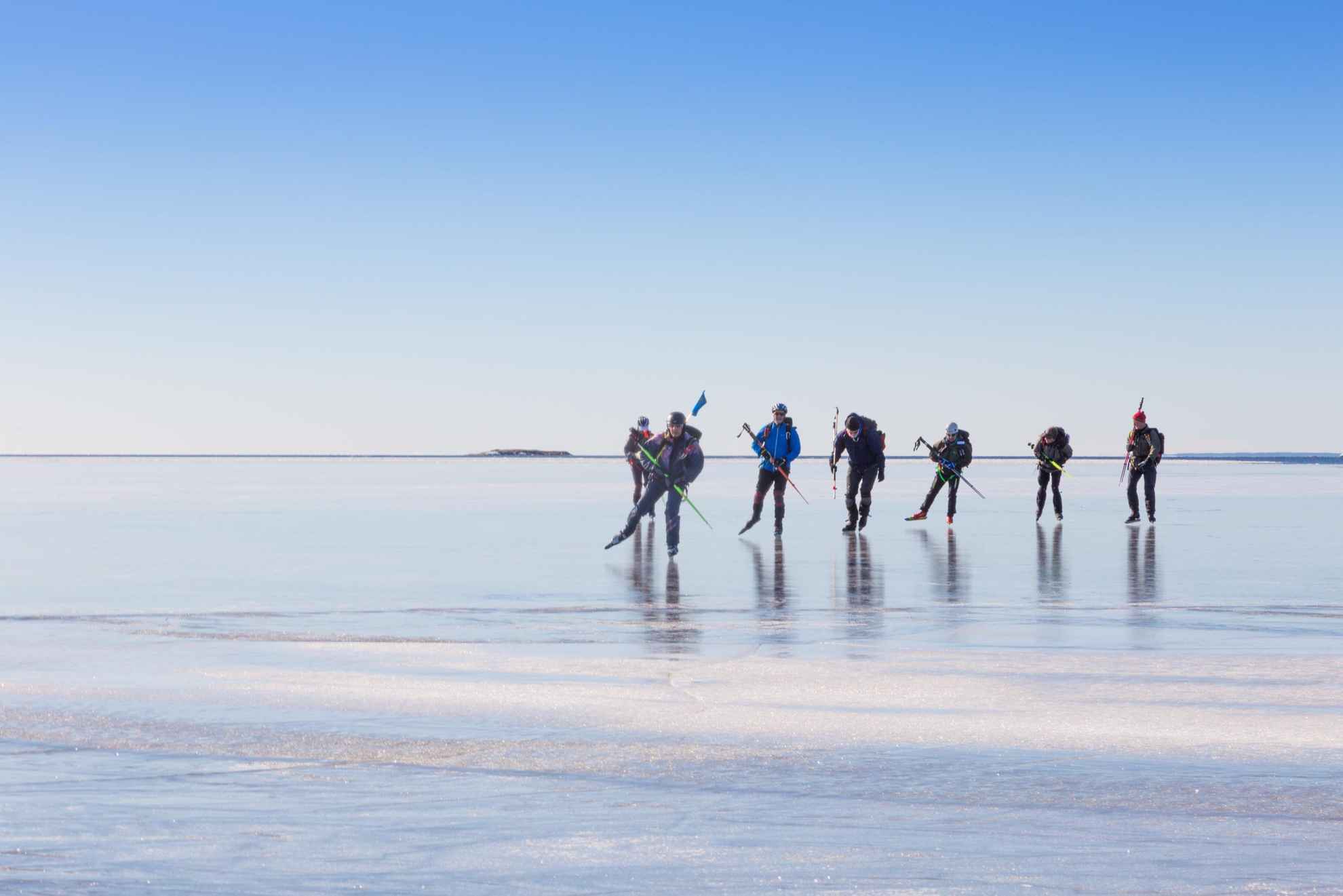Sieben Personen laufen an einem sonnigen Wintertag auf dem klaren Eis eines Sees.
