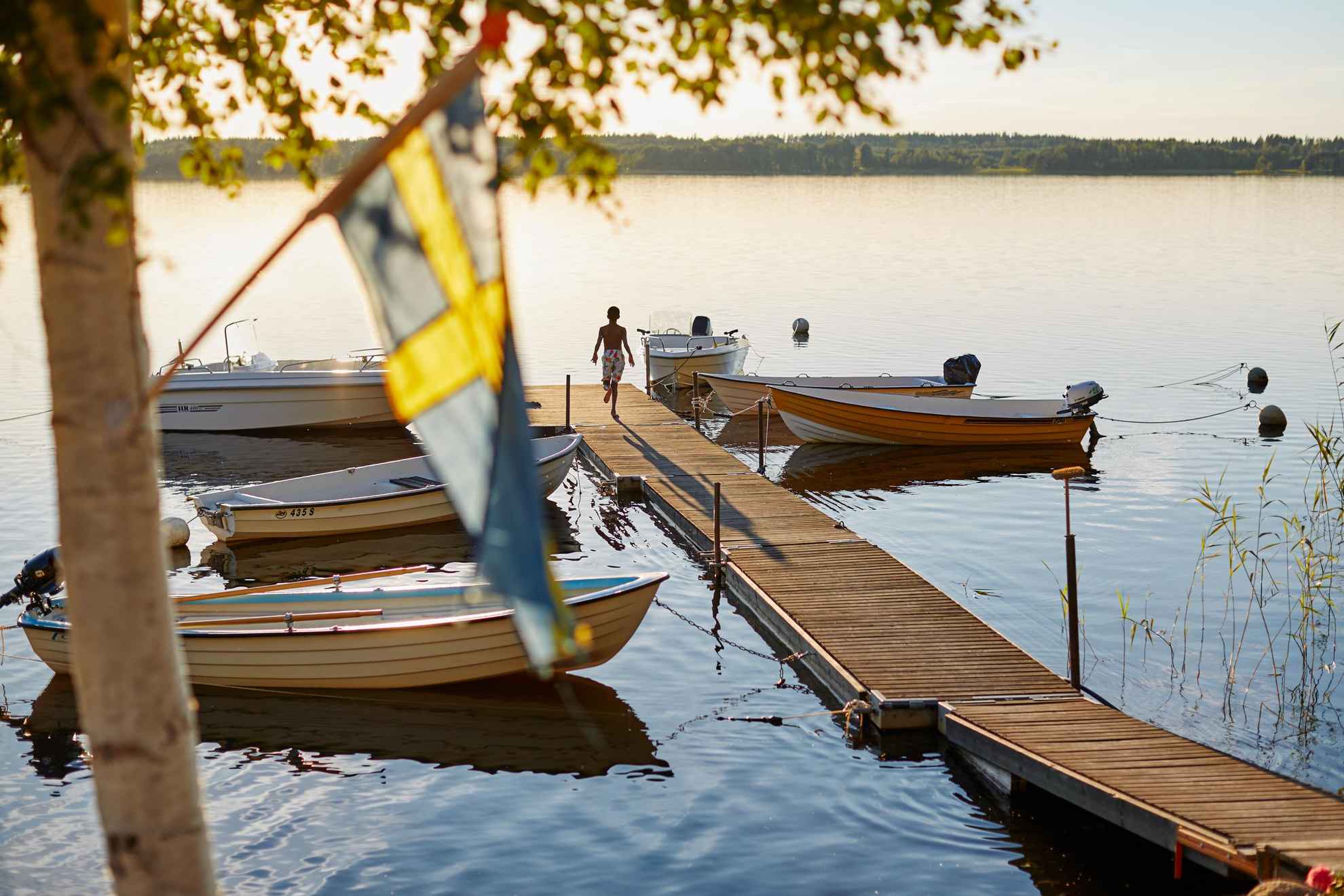 Eine Person läuft über einen Steg an einem schwedischen See. Man kann eine Schwedenflagge und ein Boot sehen.