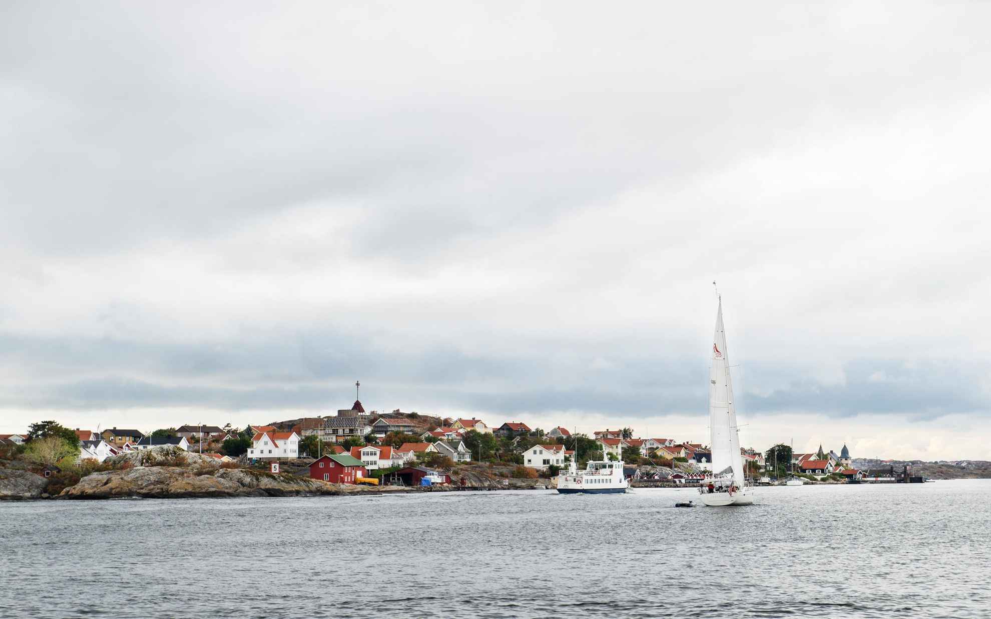 Eine kleine Fähre und ein Segelboot im Meer, vorbei an einer Insel mit vielen Häusern außerhalb von Göteborg.