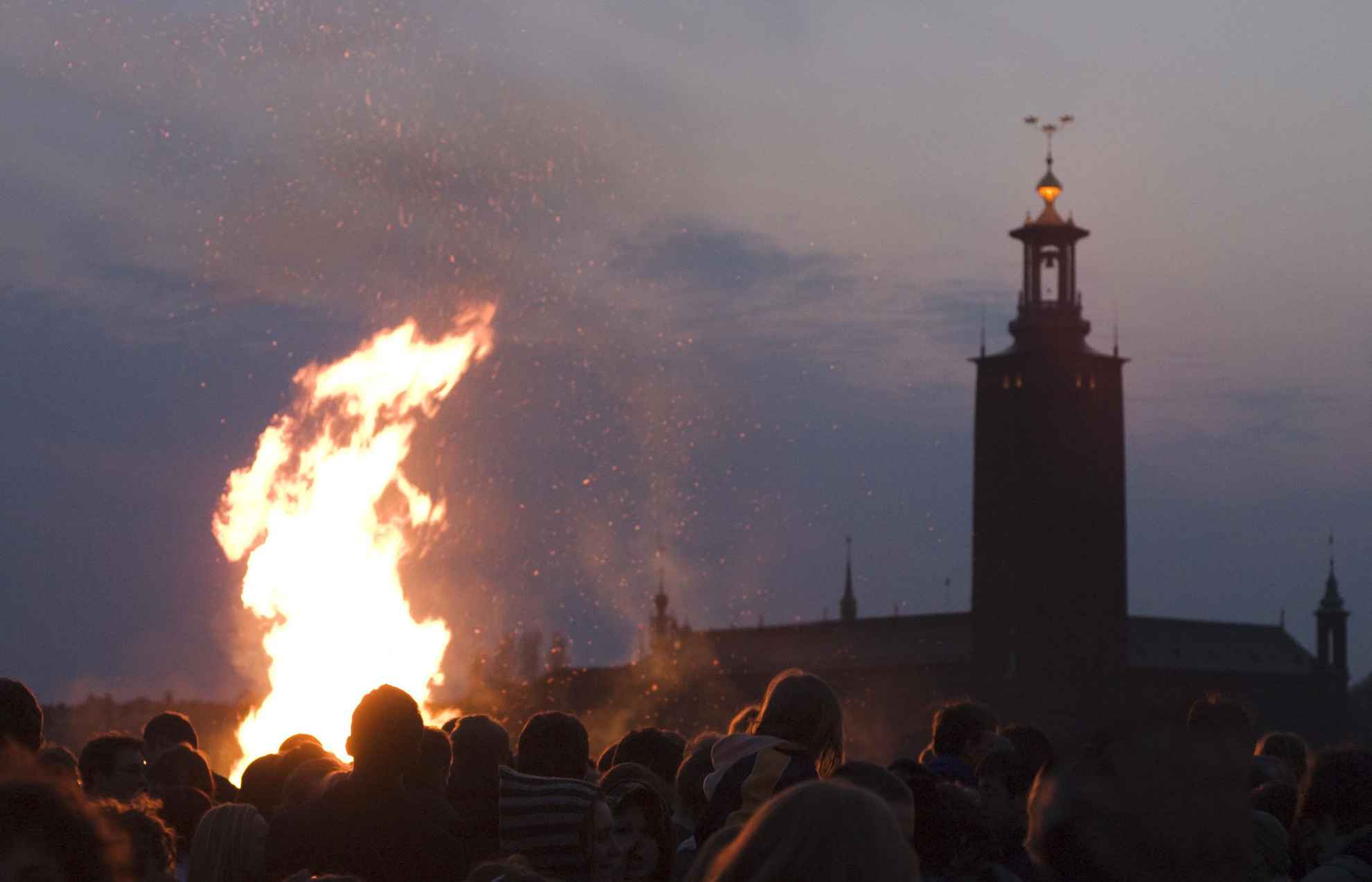 Menschen stehen um ein Lagerfeuer.  Im Hintergrund das Rathaus von Stockholm.