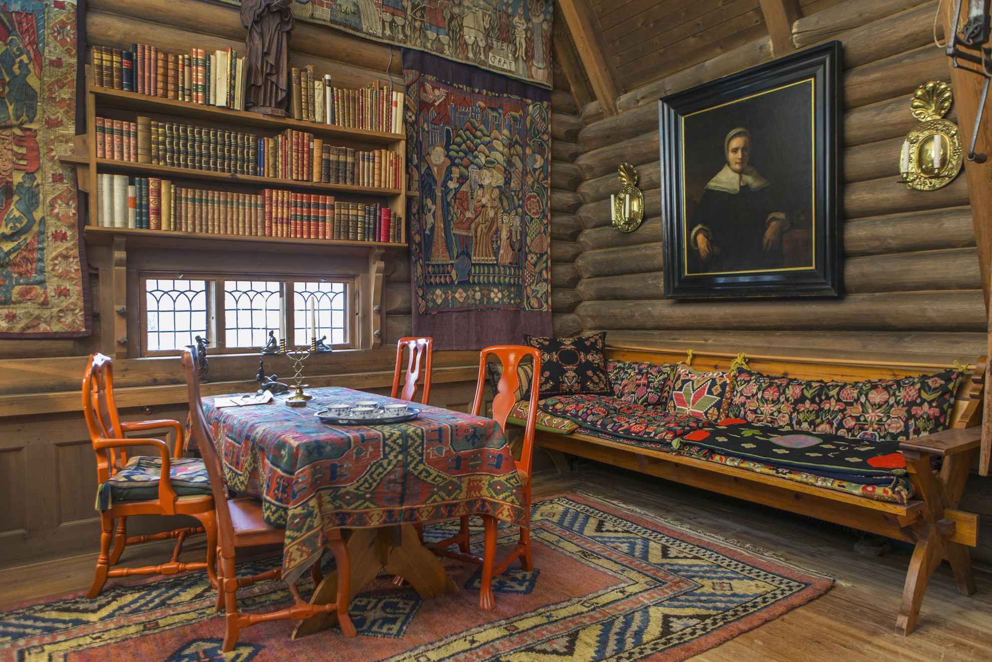 Ein Raum aus Holzwänden mit einem Esstisch und einem Gemälde sowie einer Wand voller alter Bücher.