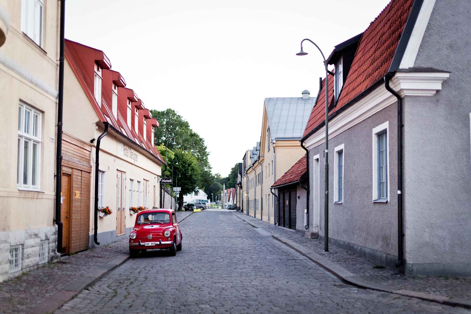 Neben den bunten Häusern Visbys. steht ein rotes Auto.