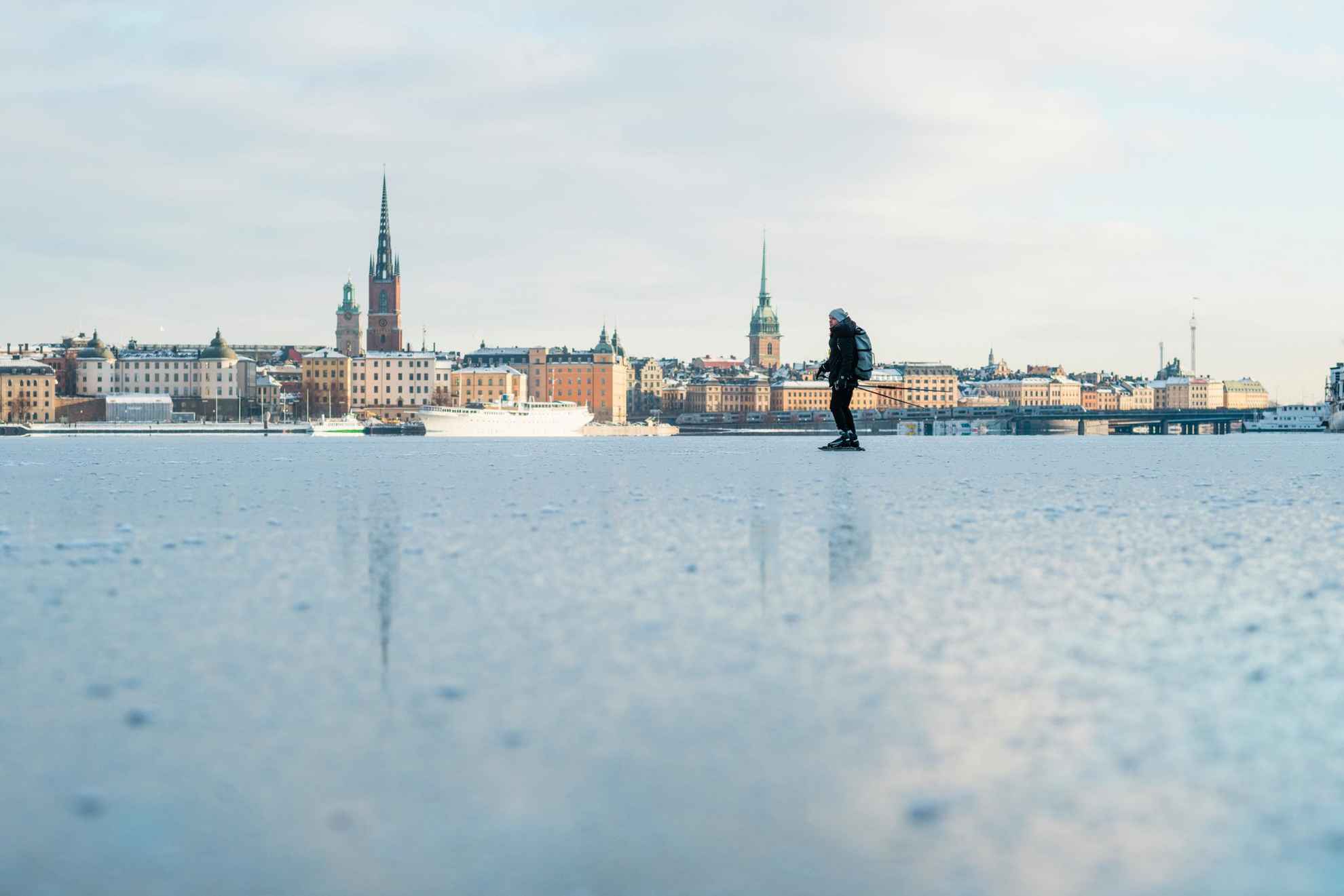 Ein Person läuft Eis auf einem zugefrorenen See, im Hintergrund die Skyline der Stockholmer Innenstadt.