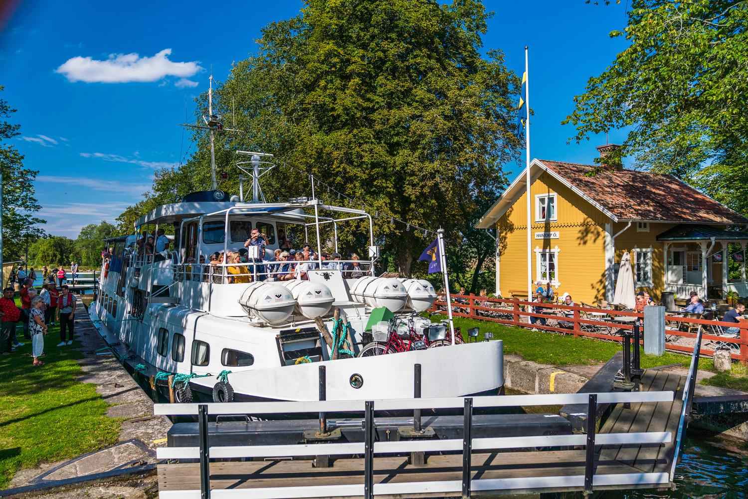 Ein großes weißes Boot fährt an dem gelben Holzhaus der Jugendherberge und des Cafés Hajstorp vorbei.