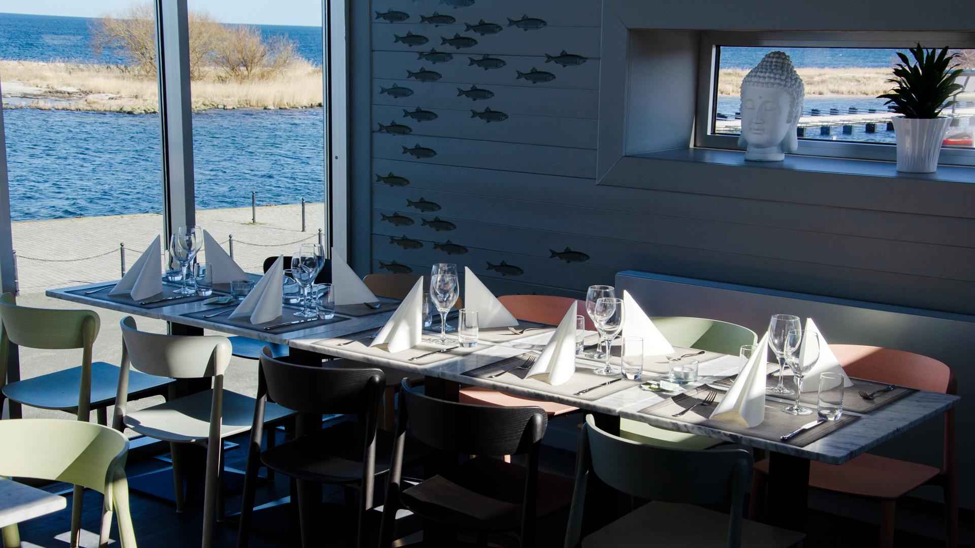 A set table at Buhres restaurant in Kivik harbour. A shoal of fish is painted on the wall, and the blue water is just outside the windows.