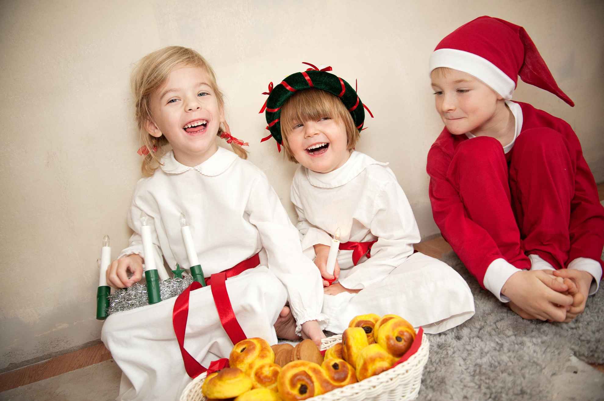 Three kids sit down, dressed as Lucia, a handmaiden and an elf or little santa.