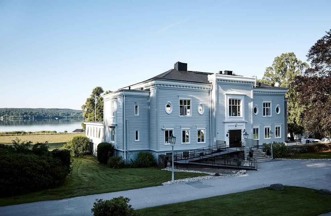 Das große graue Holzhaus, das Aspenäs Manor ist. Das Haus ist von viel Grün umgeben und liegt direkt am Aspen-See.