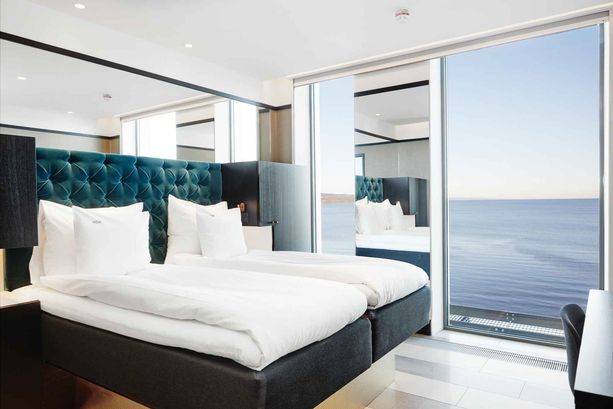 Ein Hotelzimmer mit einem Doppelbett mit weißer Bettwäsche. Das Zimmer hat große Fenster mit Blick auf den Vätternsee.