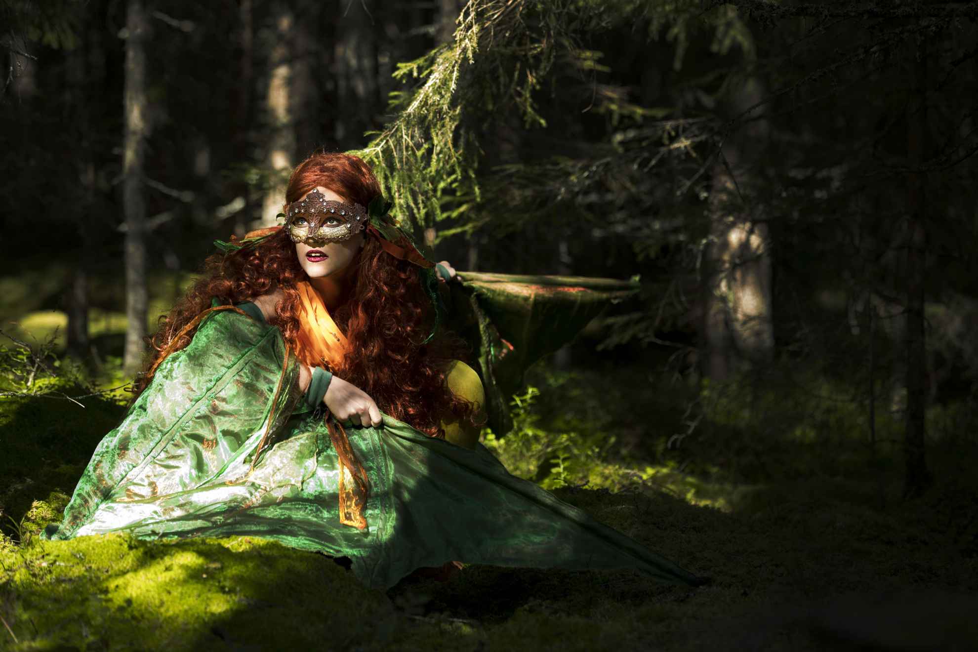 Mythical fairy dressed in green with a mask over her eyes in a lush forest