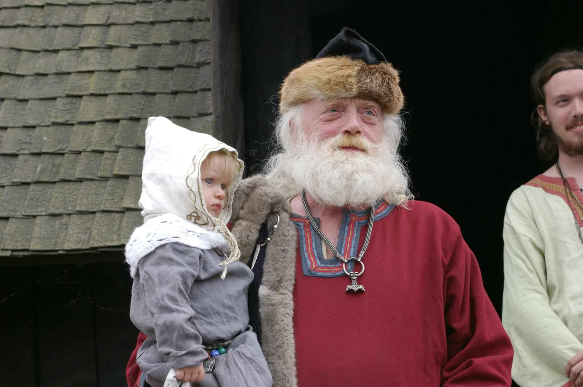Ein Mann hält ein kleines Kind, beide sind in Wikingerkleidung gekleidet.