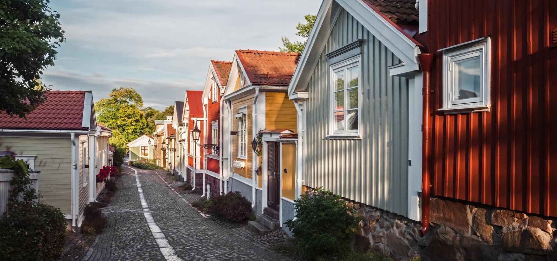Zwischen pastellfarbenen Holzhäusern erstreckt sich eine Kopfsteinpflasterstraße.