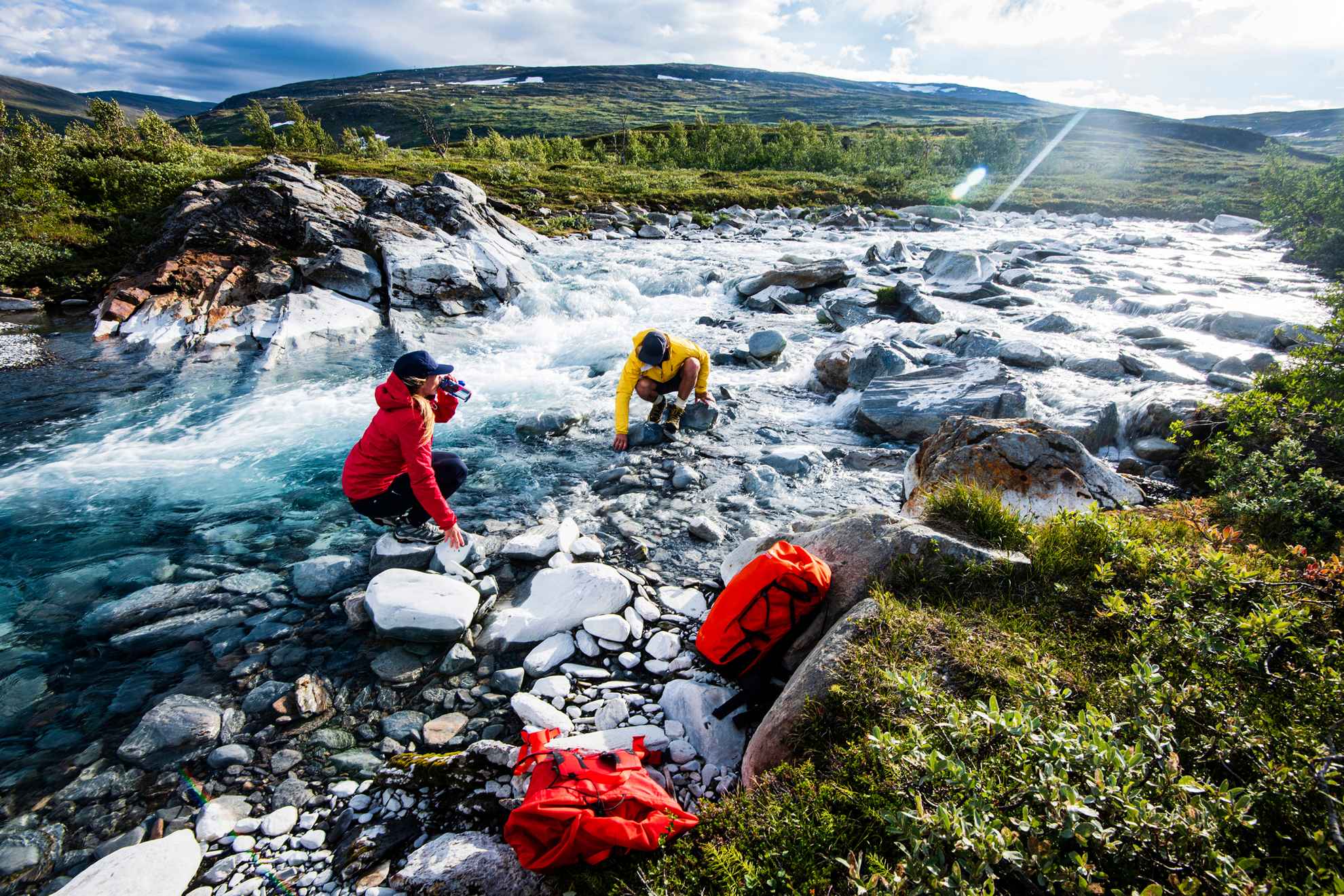 Zwei Menschen trinken aus einem Fluss in Schwedisch Lappland.