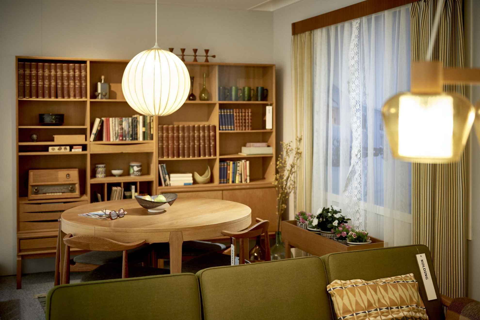 Ein altmodisches Wohnzimmer mit Schrankwand, einem runden Esstisch und im Vordergrund ein grünes Stoffsofa.